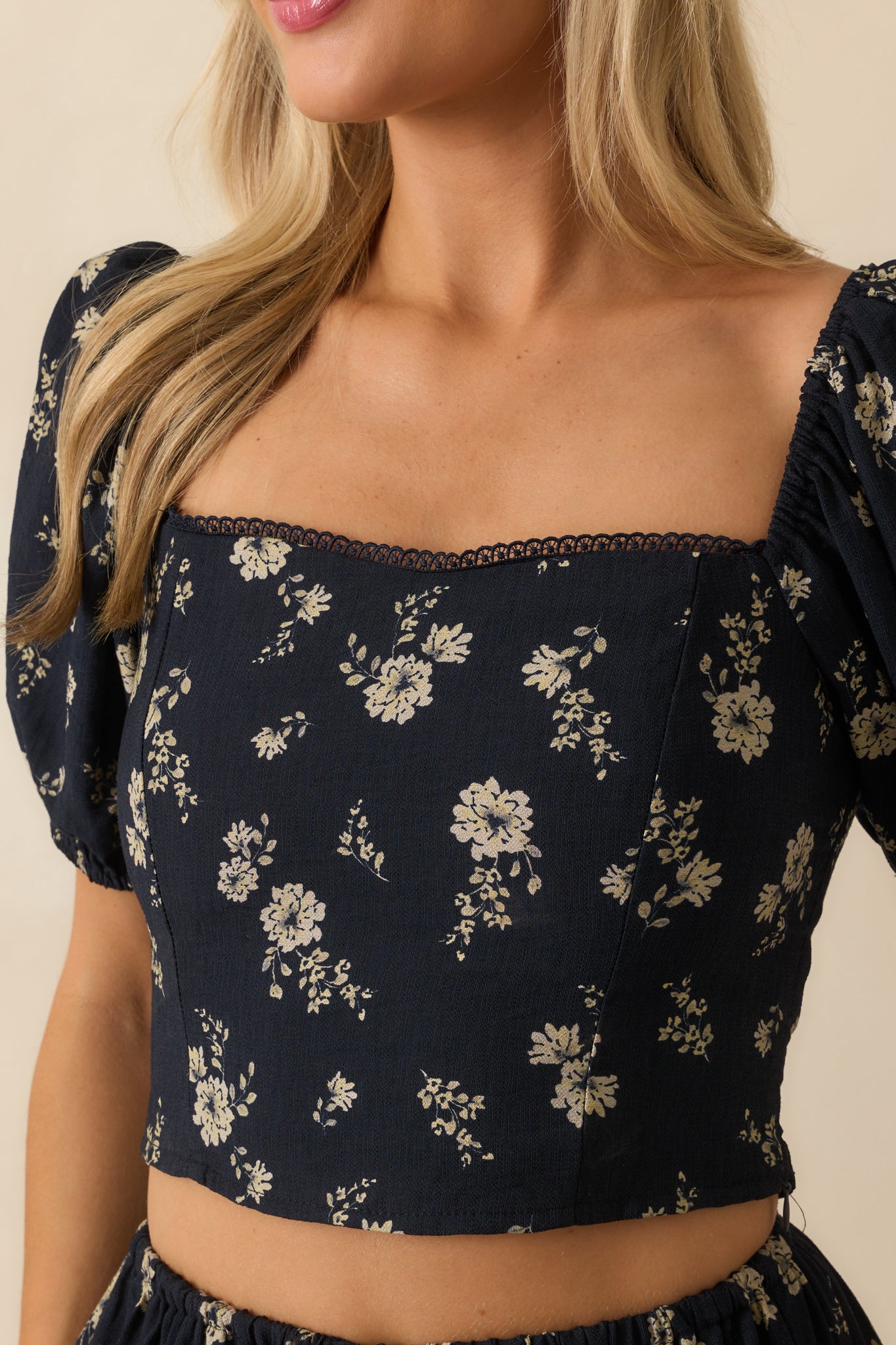 Close-up of the navy top, showing the ivory floral print, lace trim, and puff sleeve texture.