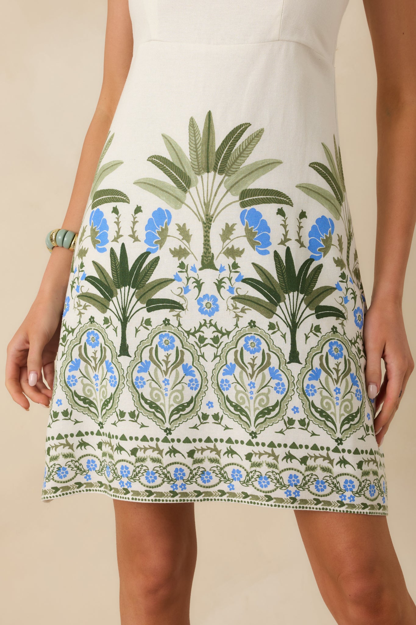 Close-up of palm and floral border print along the hem of the ivory mini dress.