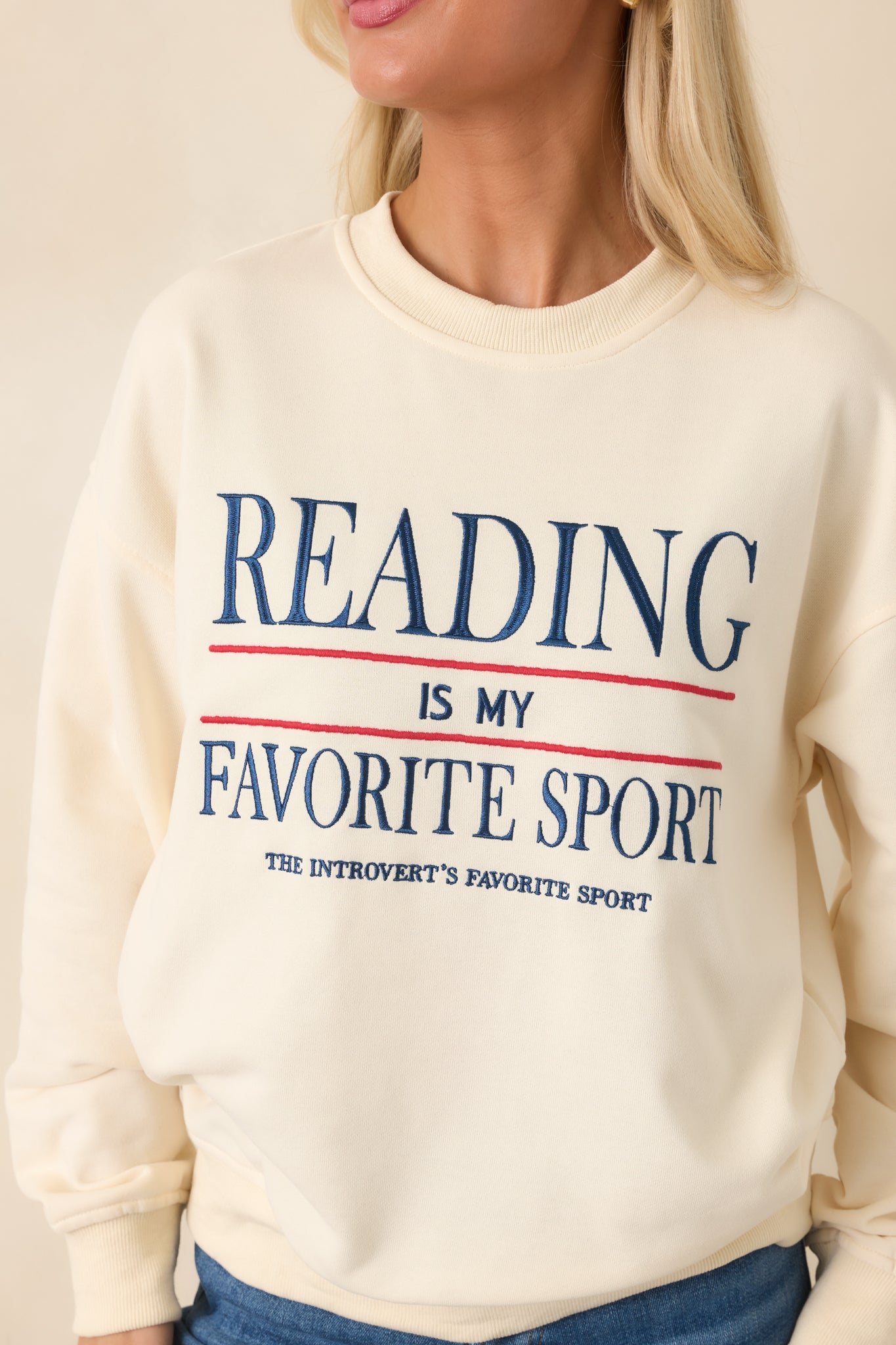 Close-up view of the embroidered navy and red lettering and textured stitching on the ivory sweatshirt.