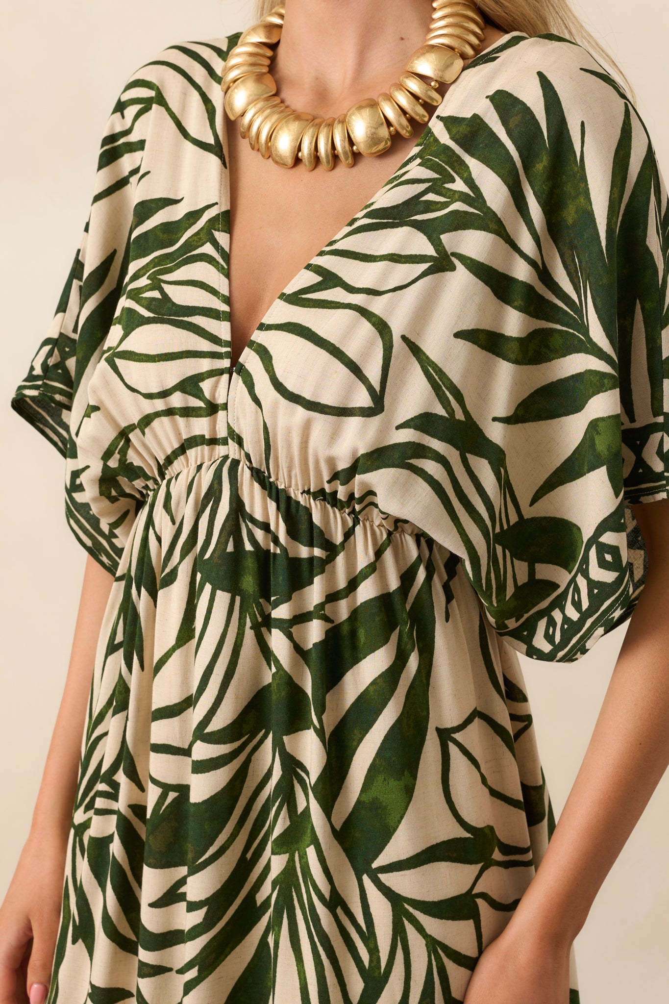 Close-up of the green and beige palm leaf print on the maxi dress, focusing on the deep V-neckline with hook-and-eye closures and the geometric hemline pattern.