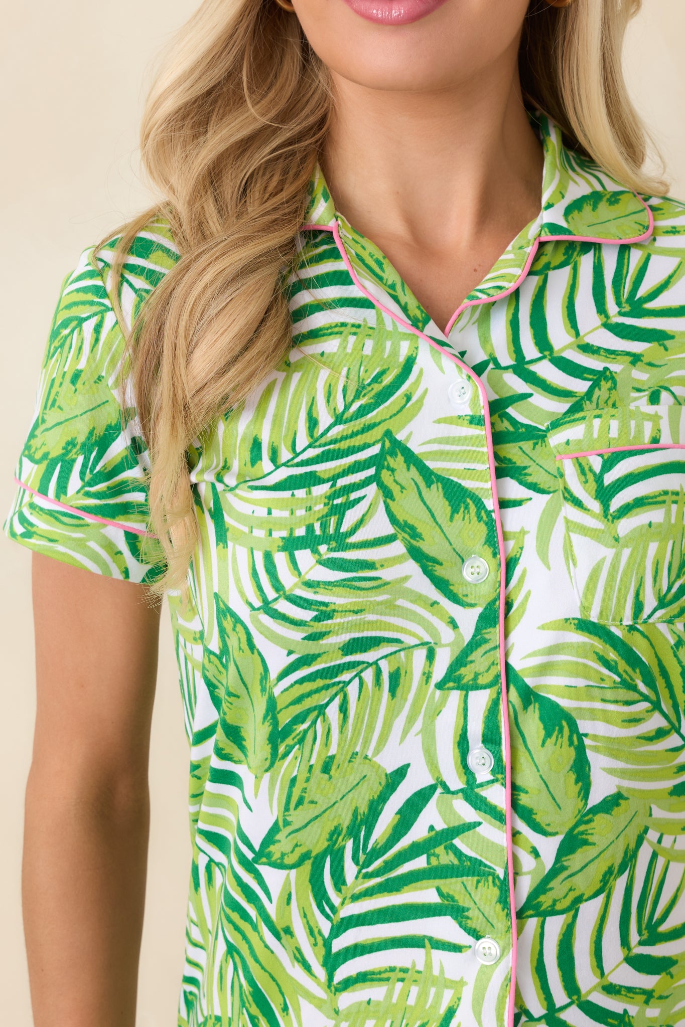 Close-up of green palm print top featuring button-front closure, pink contrast piping, and chest pocket stitching