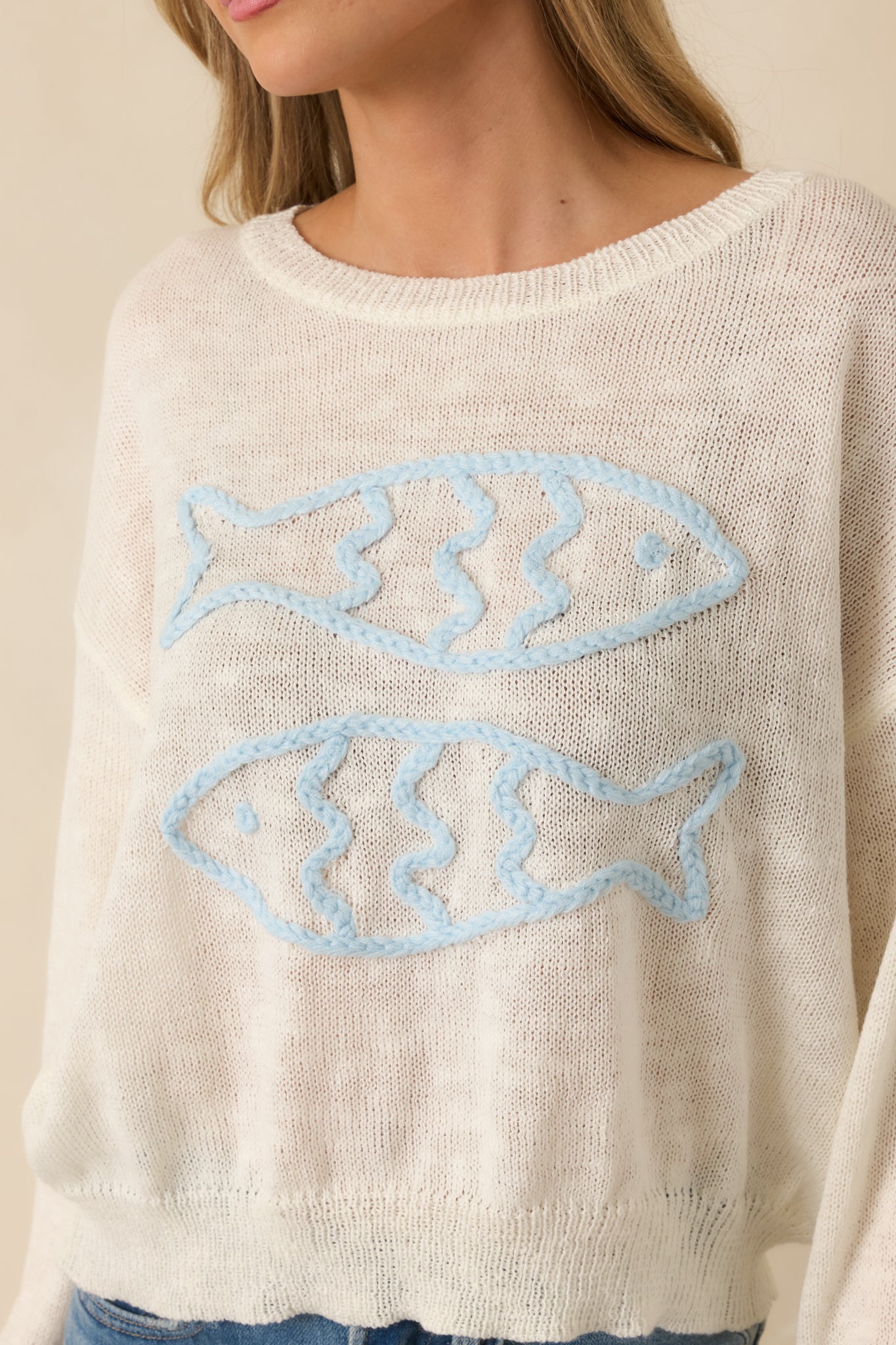 Close-up of ivory sweater showing soft knit fabric and detailed blue fish embroidery