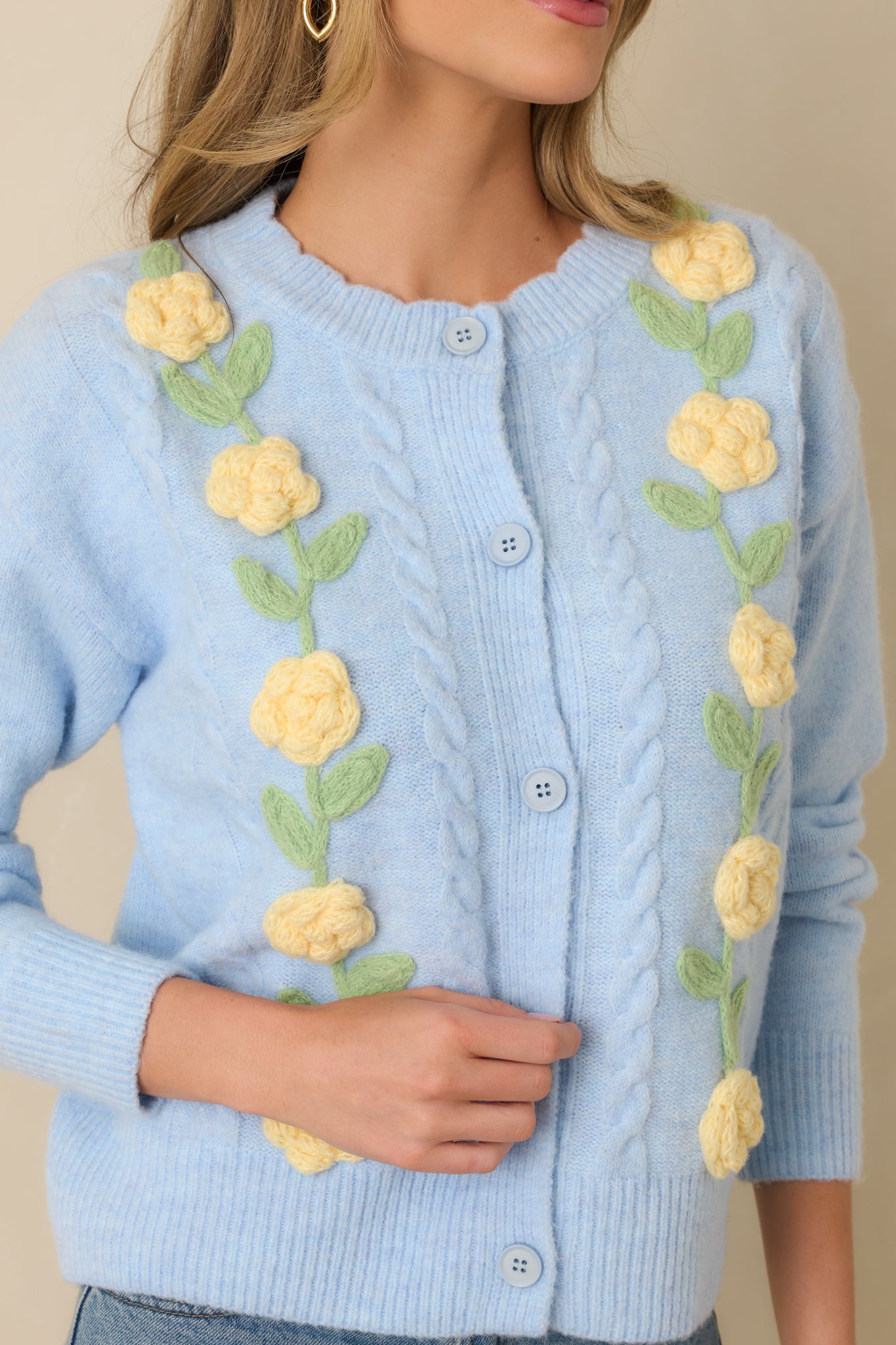 Focused close-up of raised floral appliqué and ribbed trim on light blue knit cardigan.