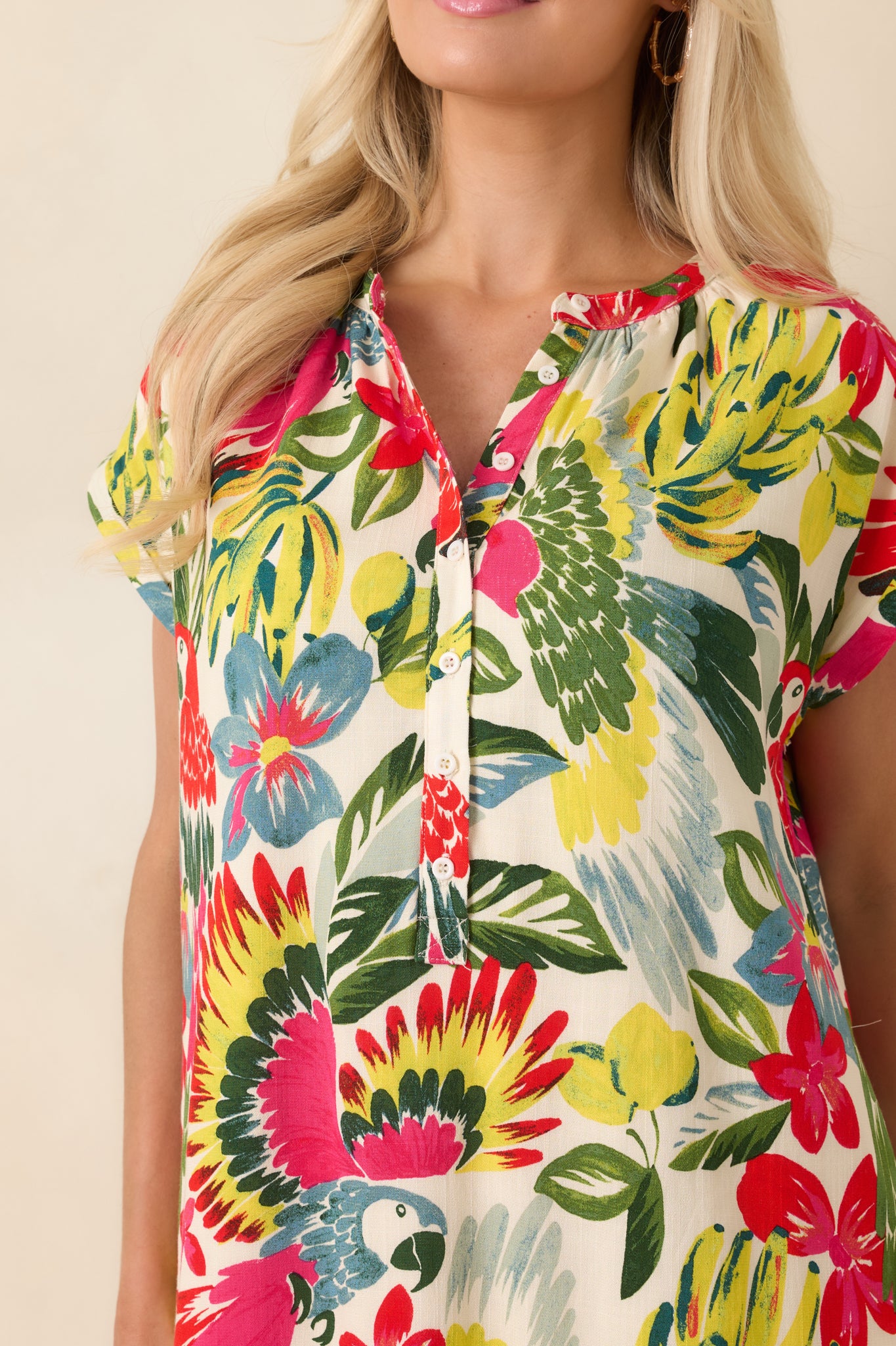 Close-up of red parrot-print mini dress featuring button-front closure, cap sleeve detail, and vibrant tropical fabric texture