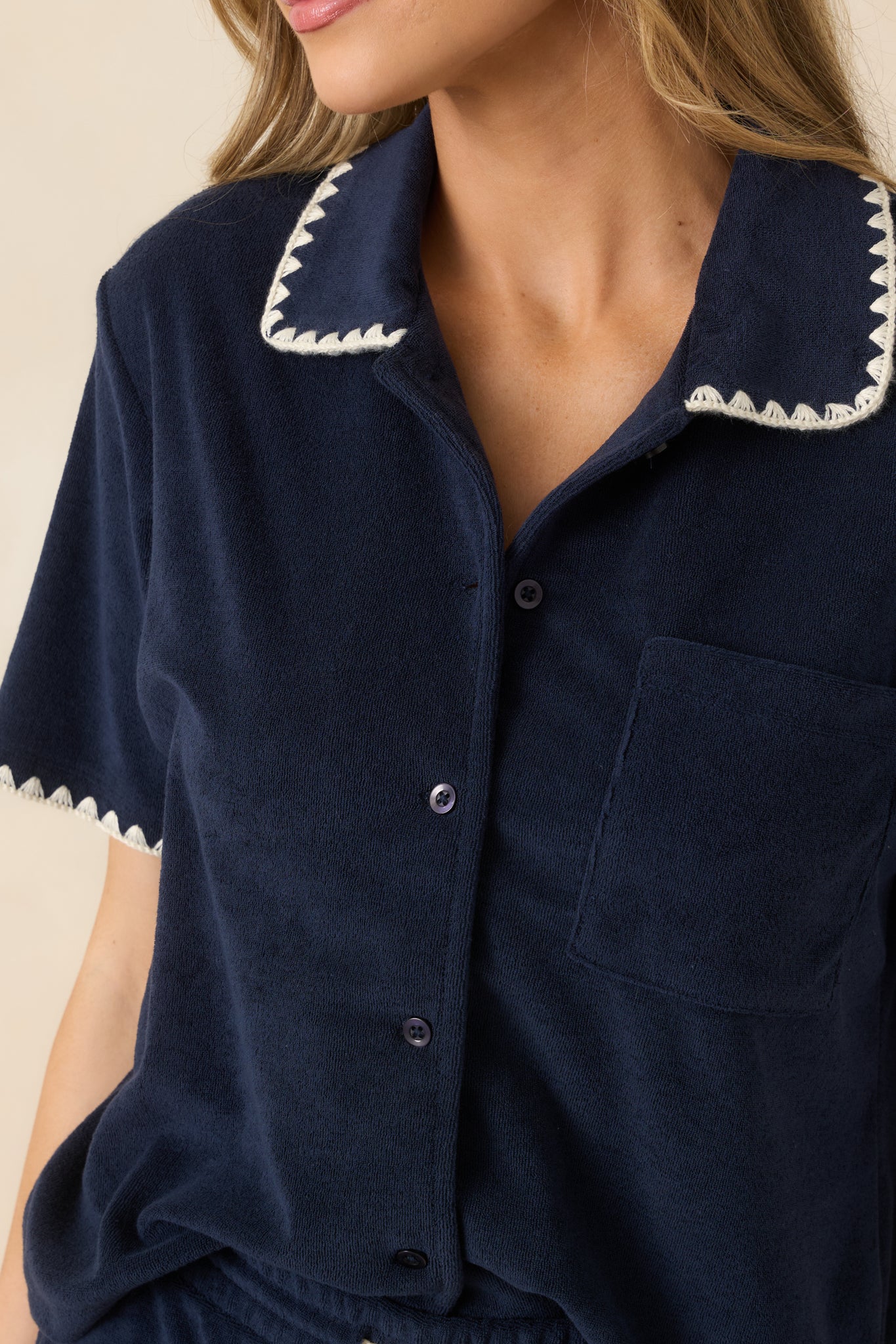 Close-up of scalloped trim detailing on collar and sleeve cuffs against rich navy loop terry fabric.