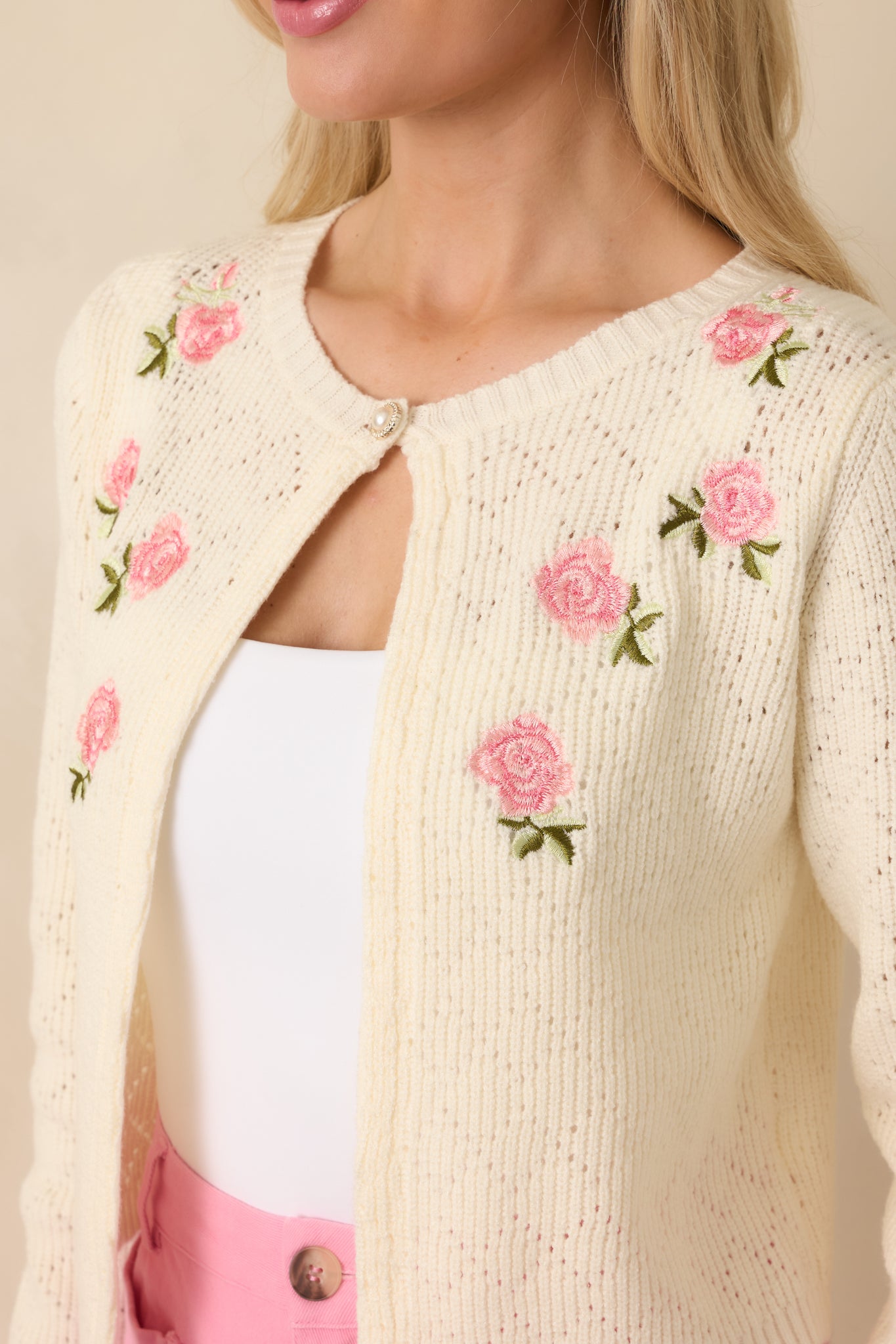 Close-up of embroidered pink rose blooms stitched into the ivory knit, featuring the pearl-style button closure for a sweet heirloom finish.