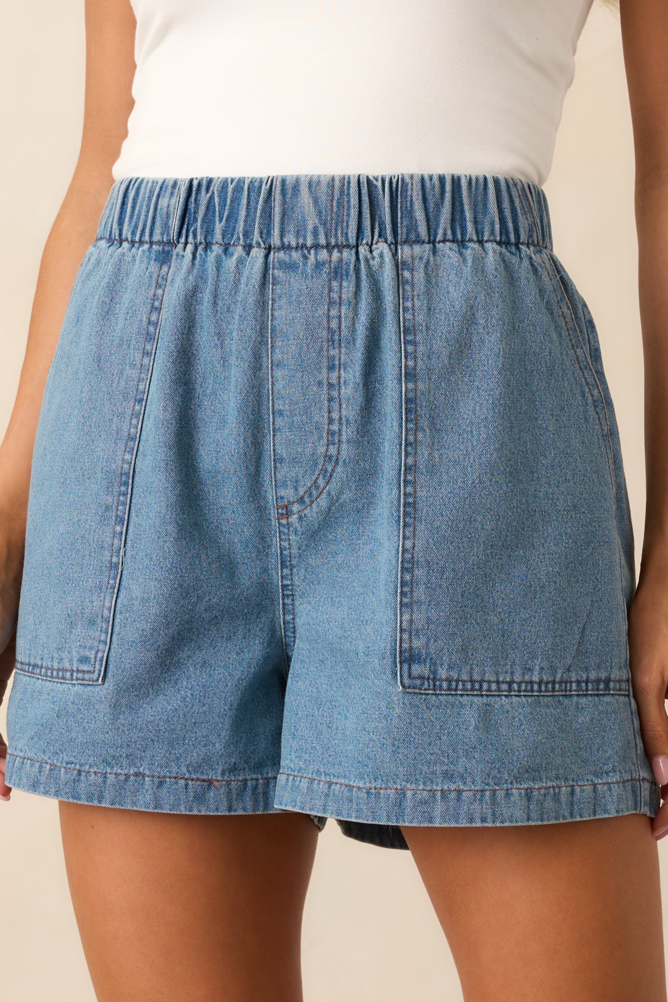 Close-up of the faux zipper closure and patch pockets on the medium wash denim shorts, highlighting the casual, relaxed look.