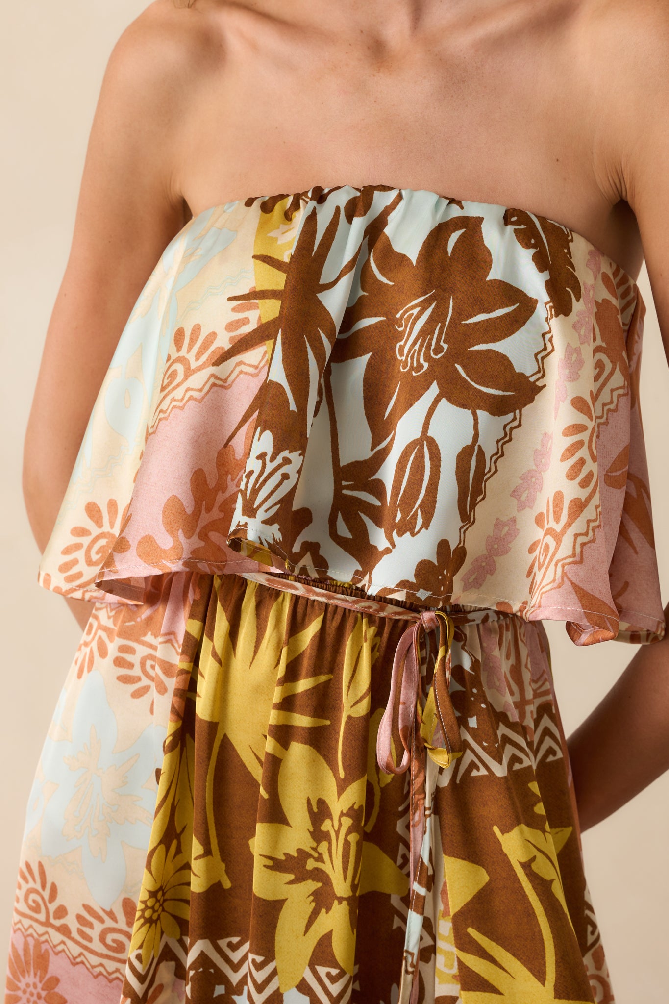 Close-up of the flounce bodice and belt area, highlighting the texture of the patchwork print, the gathered elastic neckline, and the blue tassel ends.