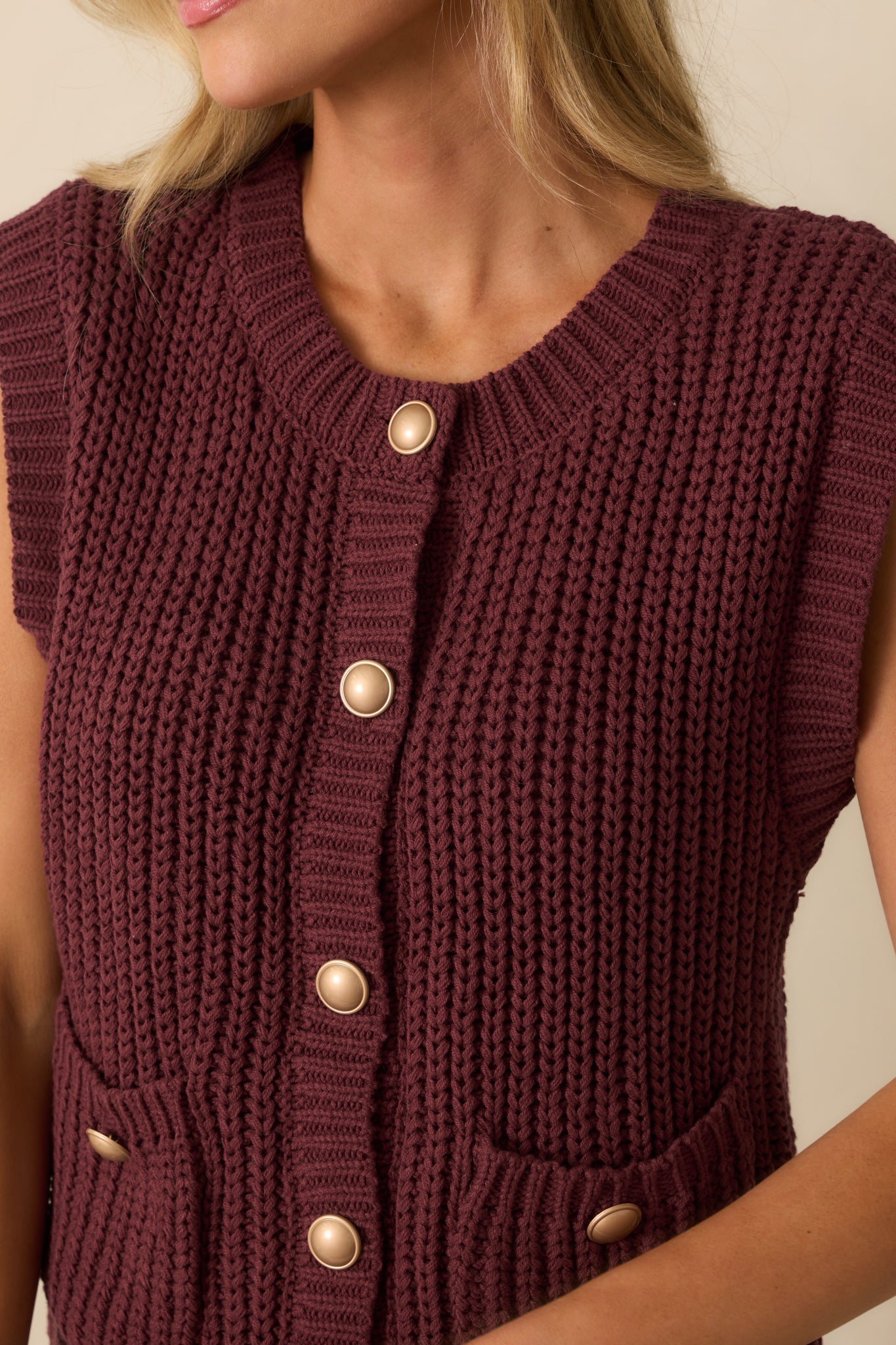 Close-up of the gold-tone buttons, ribbed knit fabric, and pocket details on the wine red sweater vest.