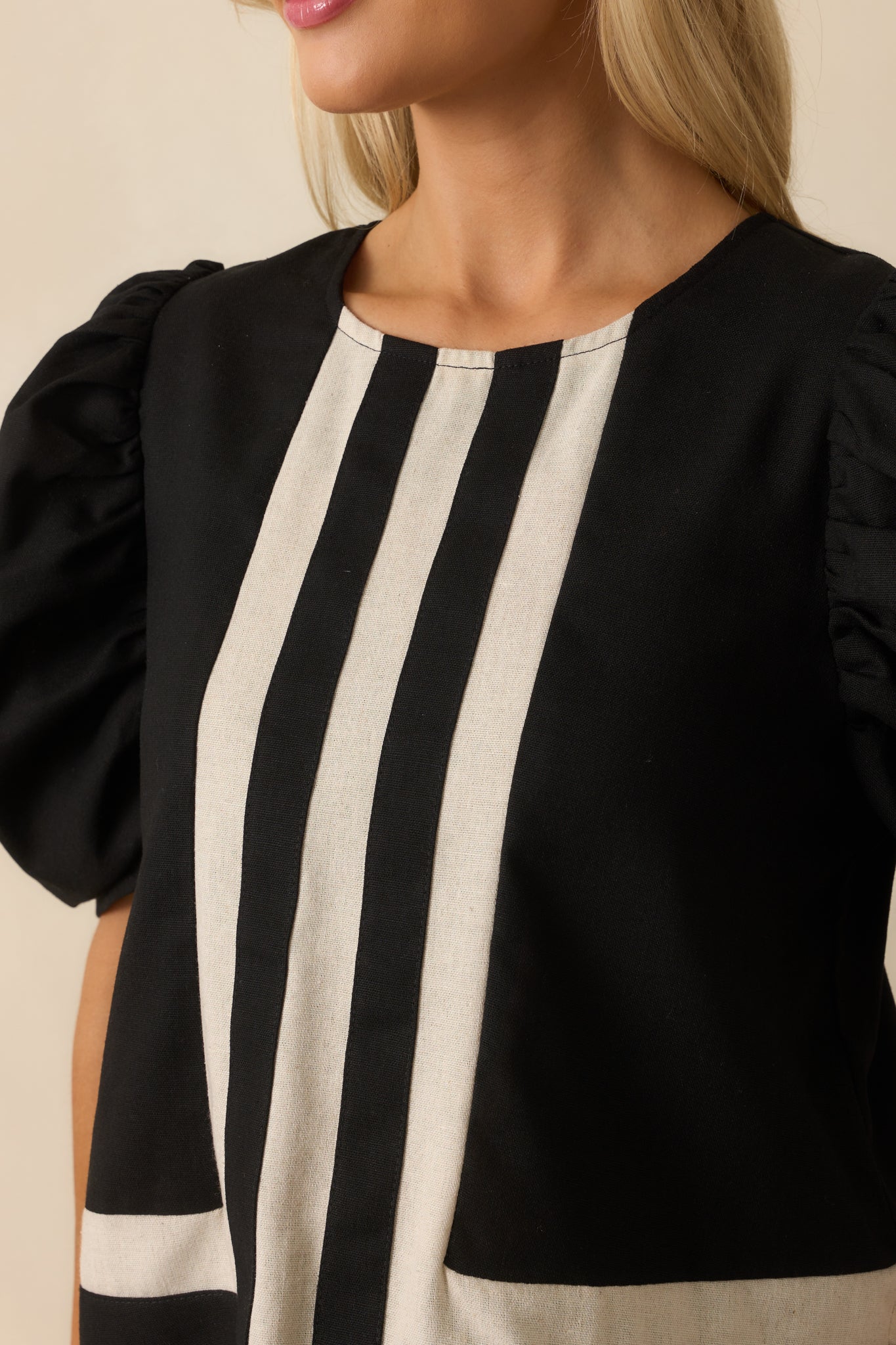 Close-up of the ivory contrast stitching and fabric texture on the black top’s front seam.