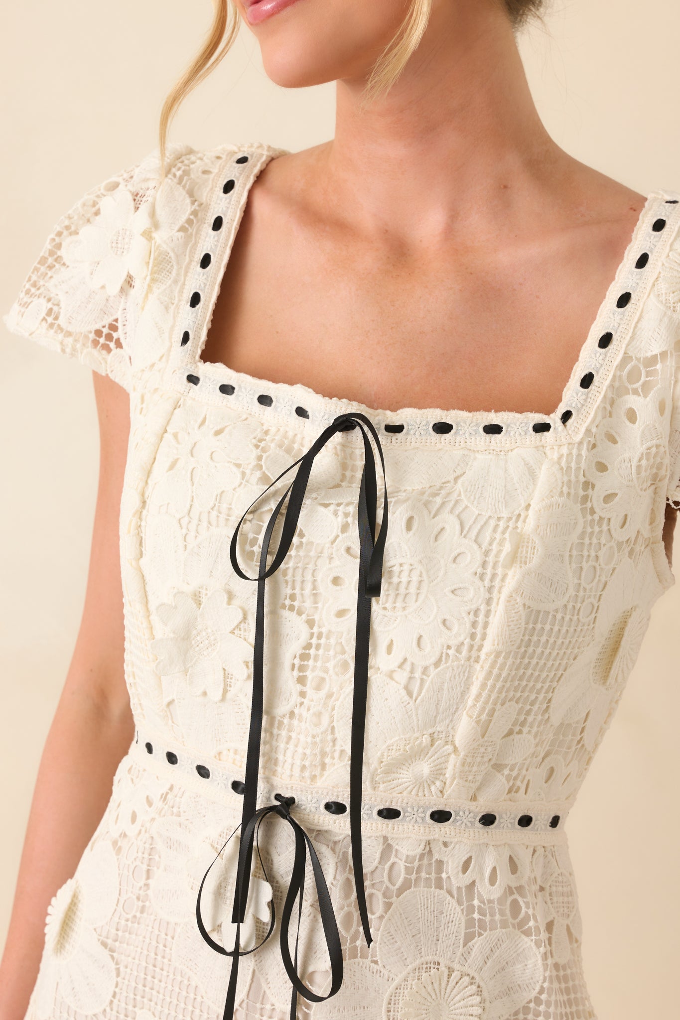 A close-up of the ivory dress, showing the embroidered sleeve design, black ribbon accents, and smooth fabric texture.