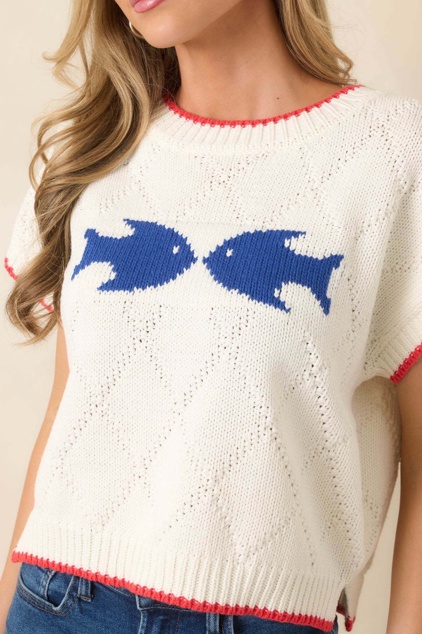 Close-up of the navy fish design, textured ivory knit, and red contrast trim along the neckline and hem.