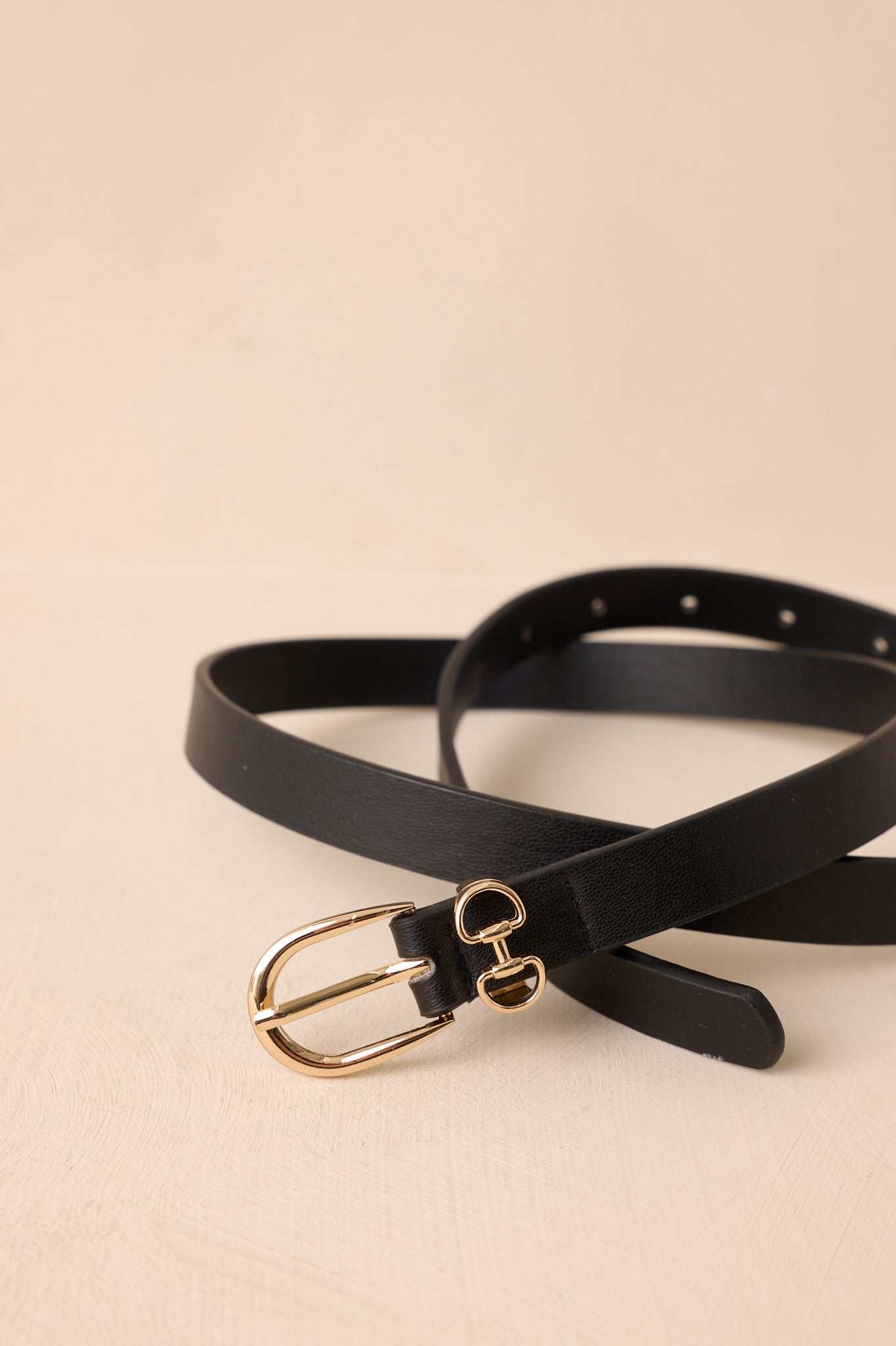 Close-up view of the polished gold horseshoe buckle with double ring accents, showing the fine texture of the black faux leather and matching belt keepers.