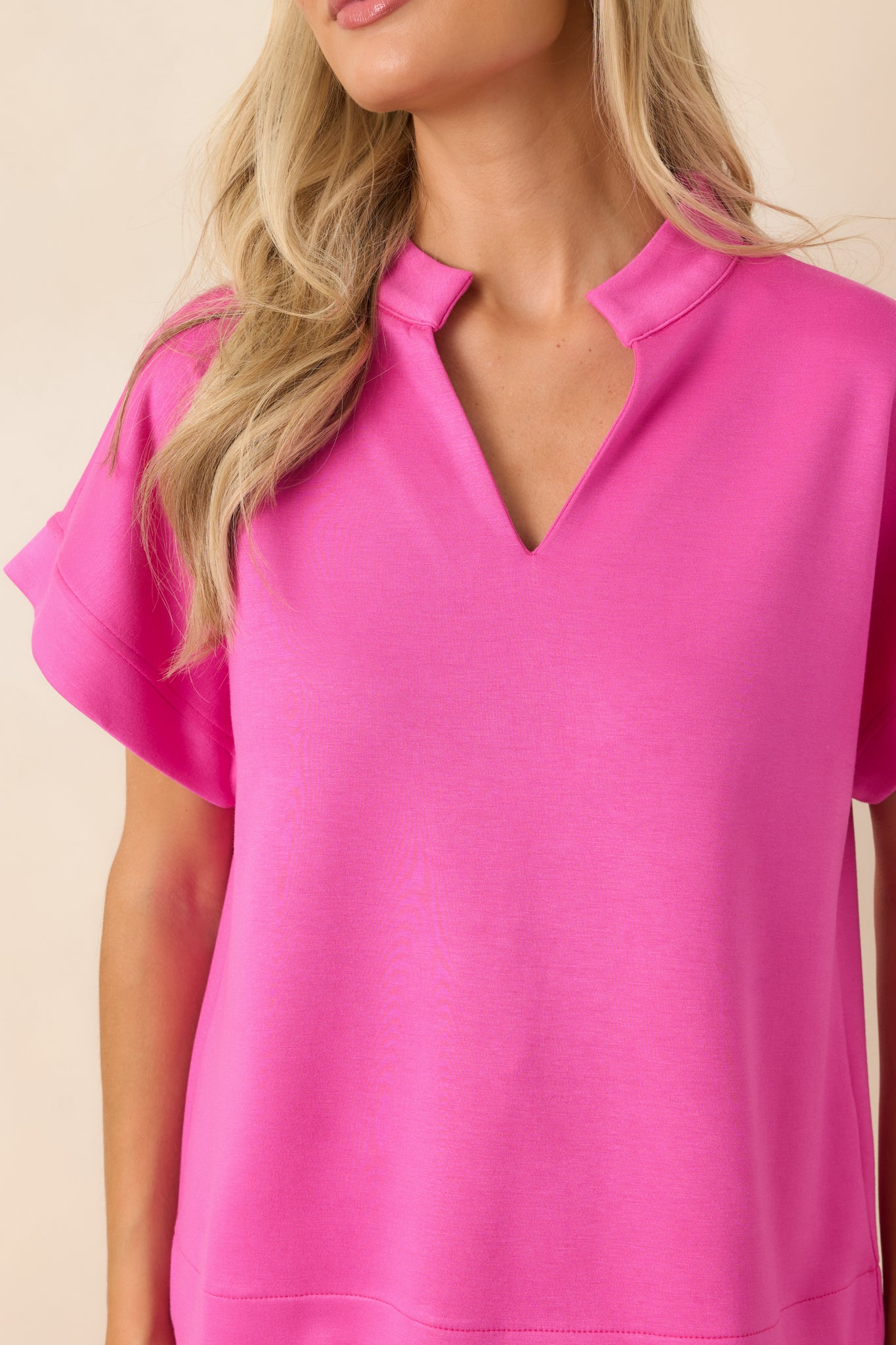 Close-up of the hot pink top featuring the structured fabric texture, split neckline, standing collar, and sleeve details.