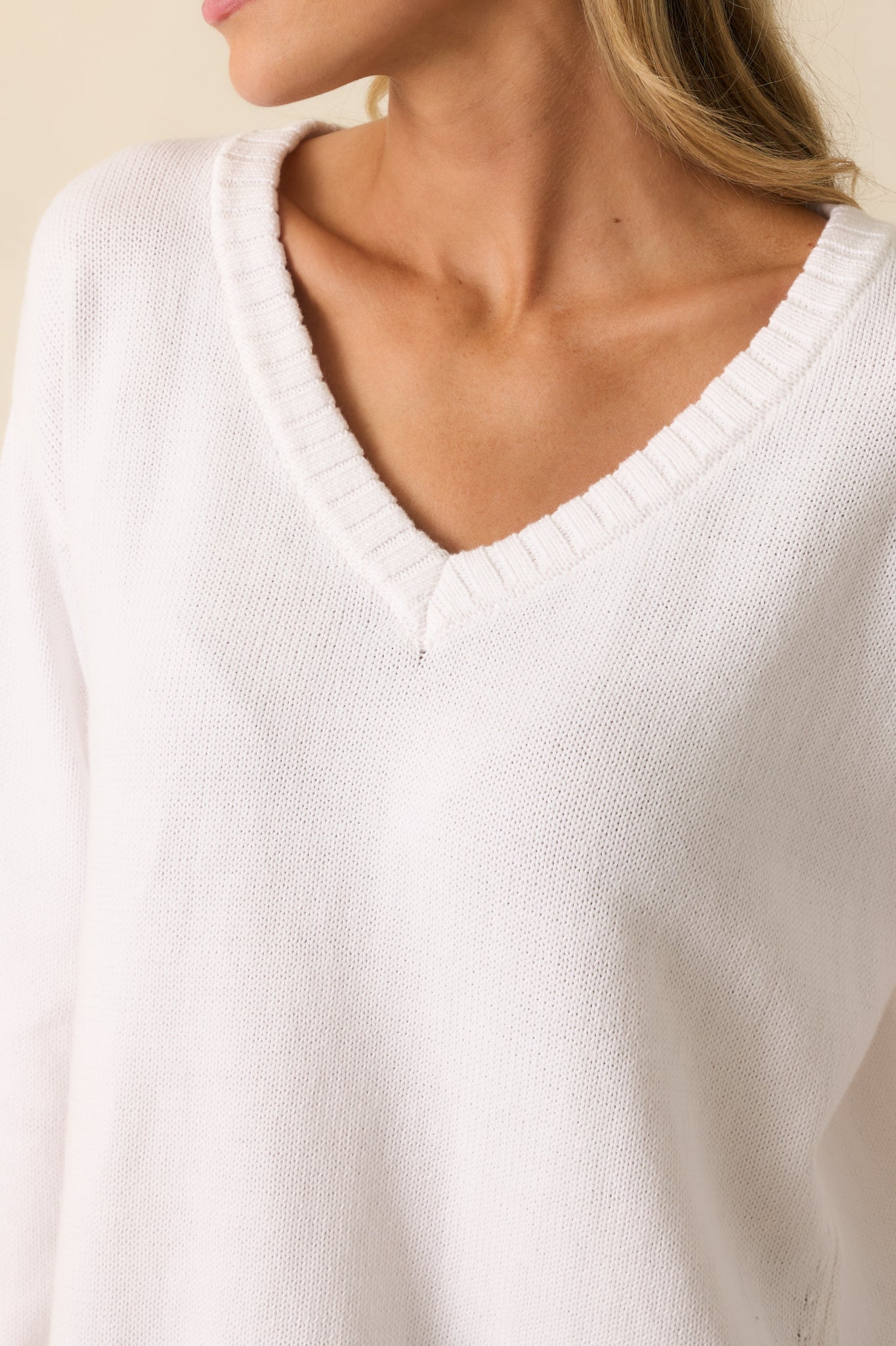 Close-up of v-neckline and ribbed hem on white cotton knit fabric.