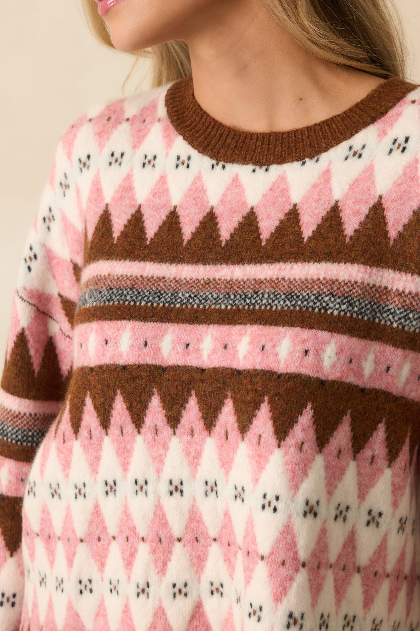 A close-up of the sweater showing pink, brown, and ivory argyle Fair Isle knit with fine geometric texture.