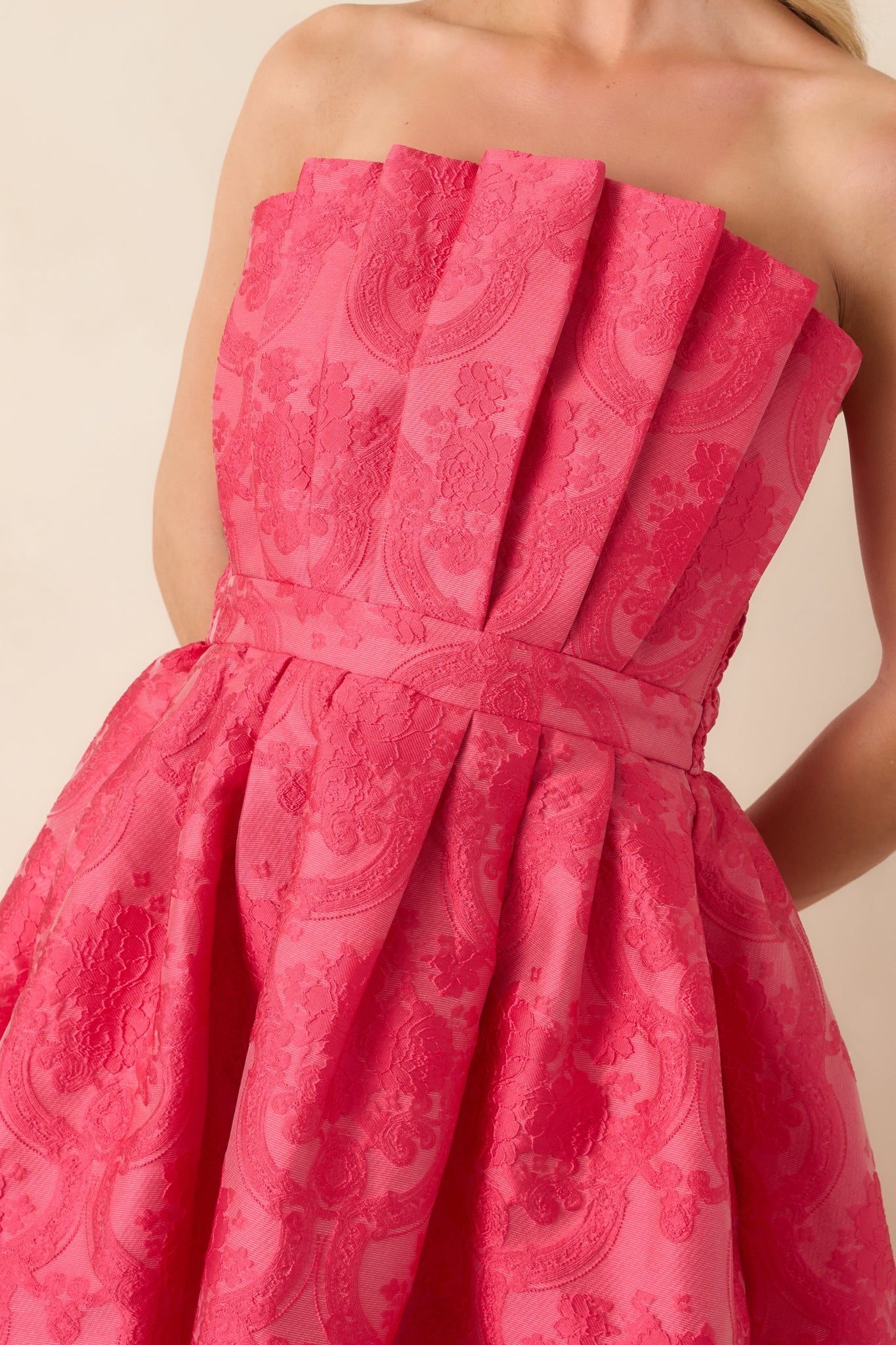 Close-up of pink strapless dress highlighting the pleated bodice, jacquard fabric texture, and pocket detail.