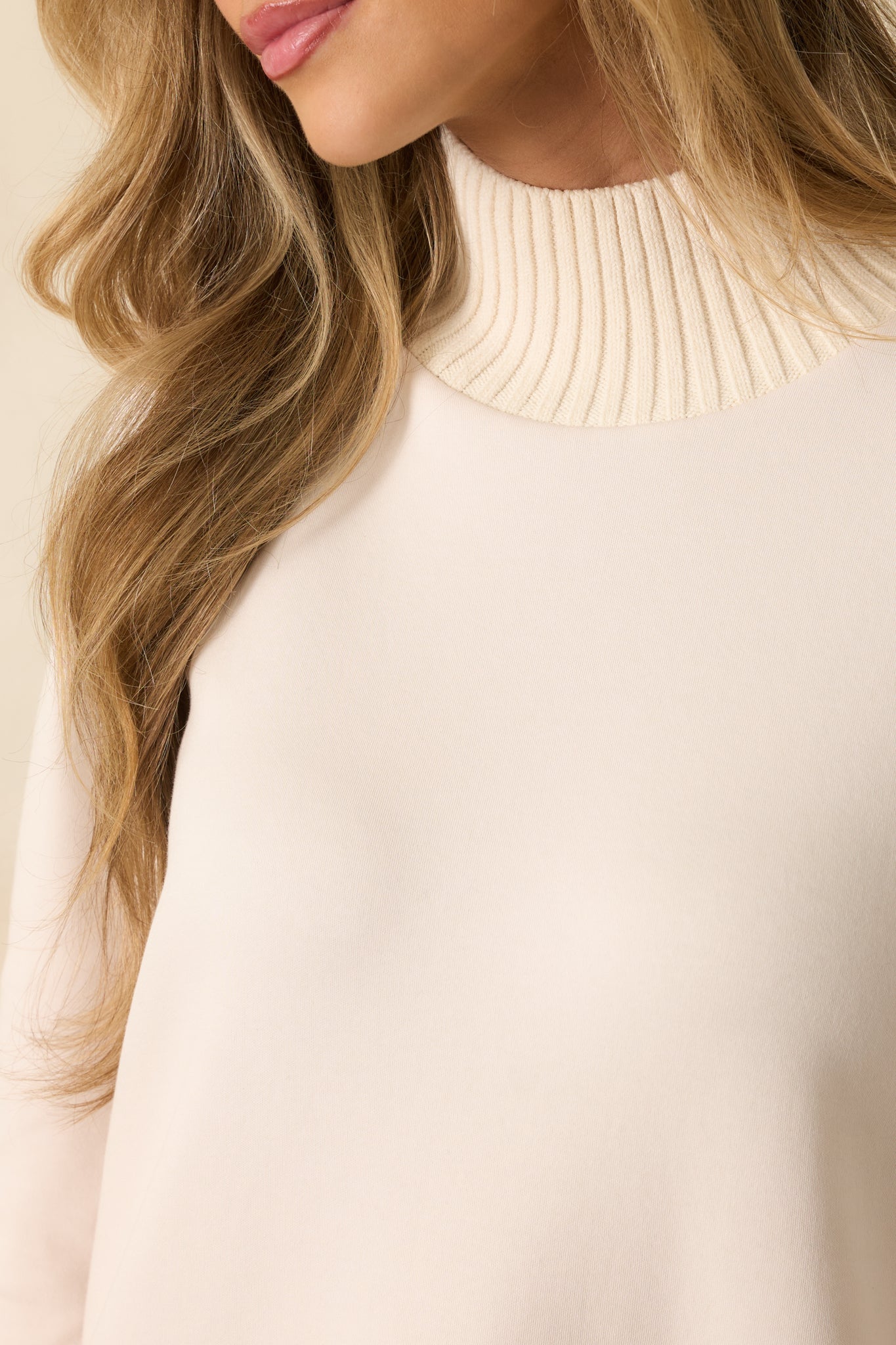 Close-up of ribbed mock neckline and fine knit texture on ivory sweater.
