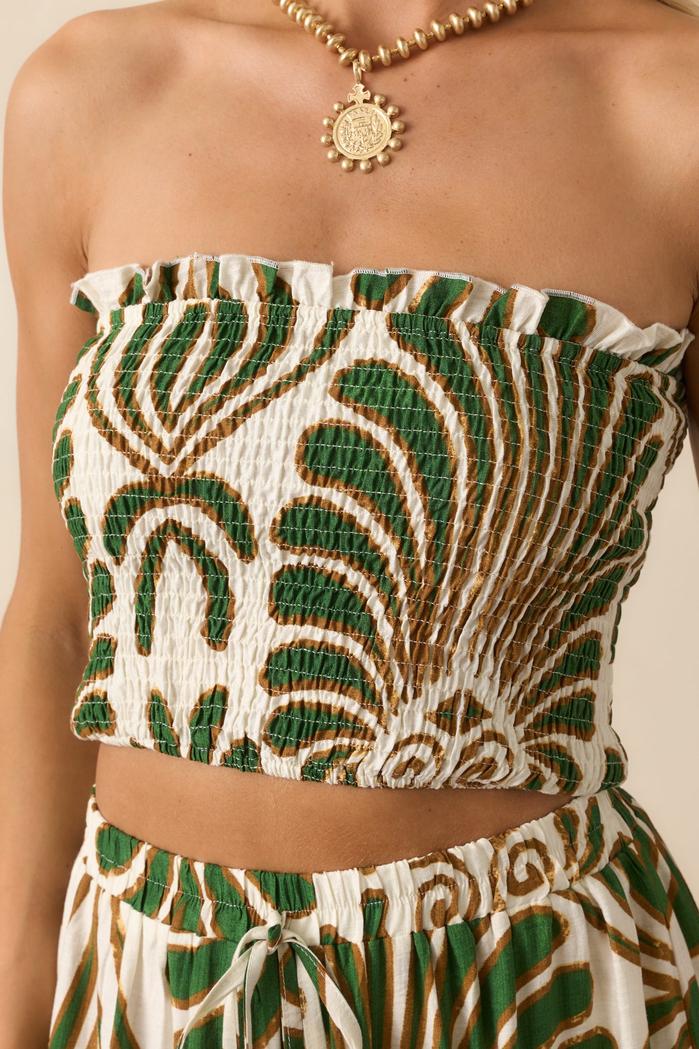 Close-up of the fabric texture, showcasing the dense smocking, green abstract print, and ruffled top edge.
