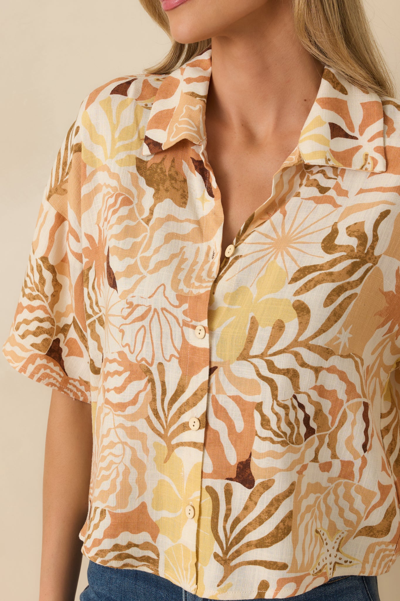 Close-up of tan tropical woven top showing button texture and intricate print design.