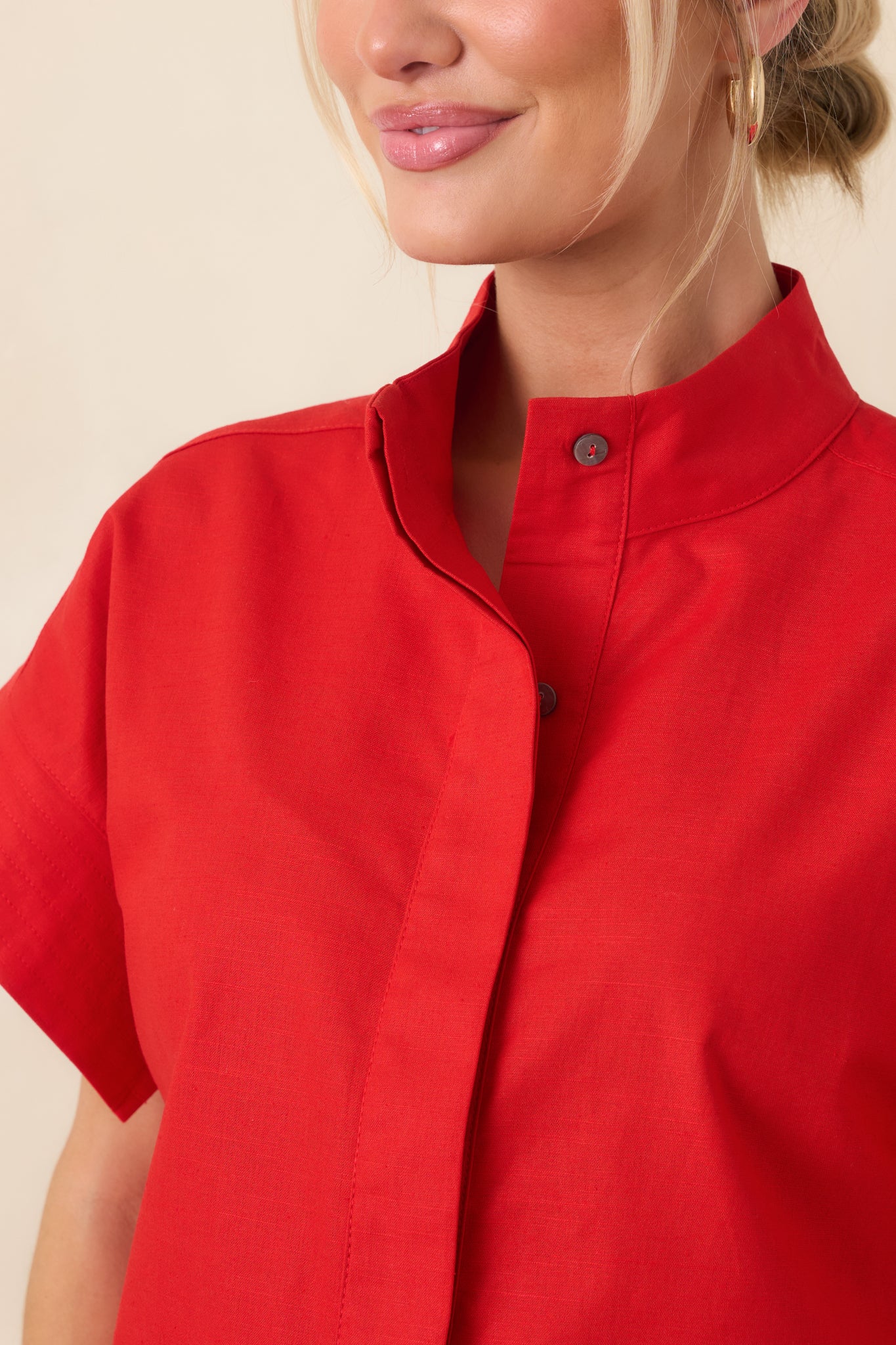 Close-up of red cotton-linen fabric showing concealed button placket and cuffed sleeve detail.