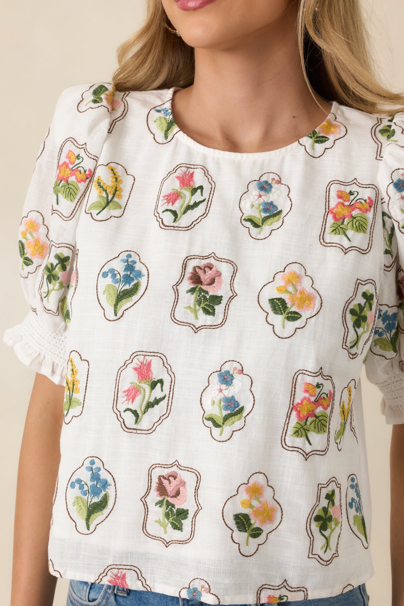 Close-up of the ivory top showing detailed multicolor floral embroidery and lightweight woven texture.
