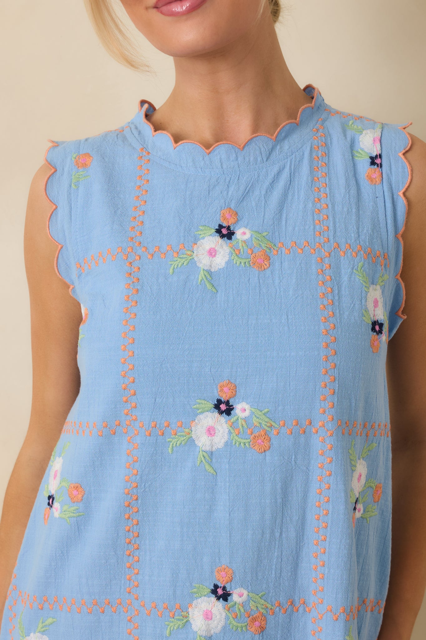 Close-up of the light blue mini dress showing the floral embroidery, decorative stitched detailing, and scalloped trim.