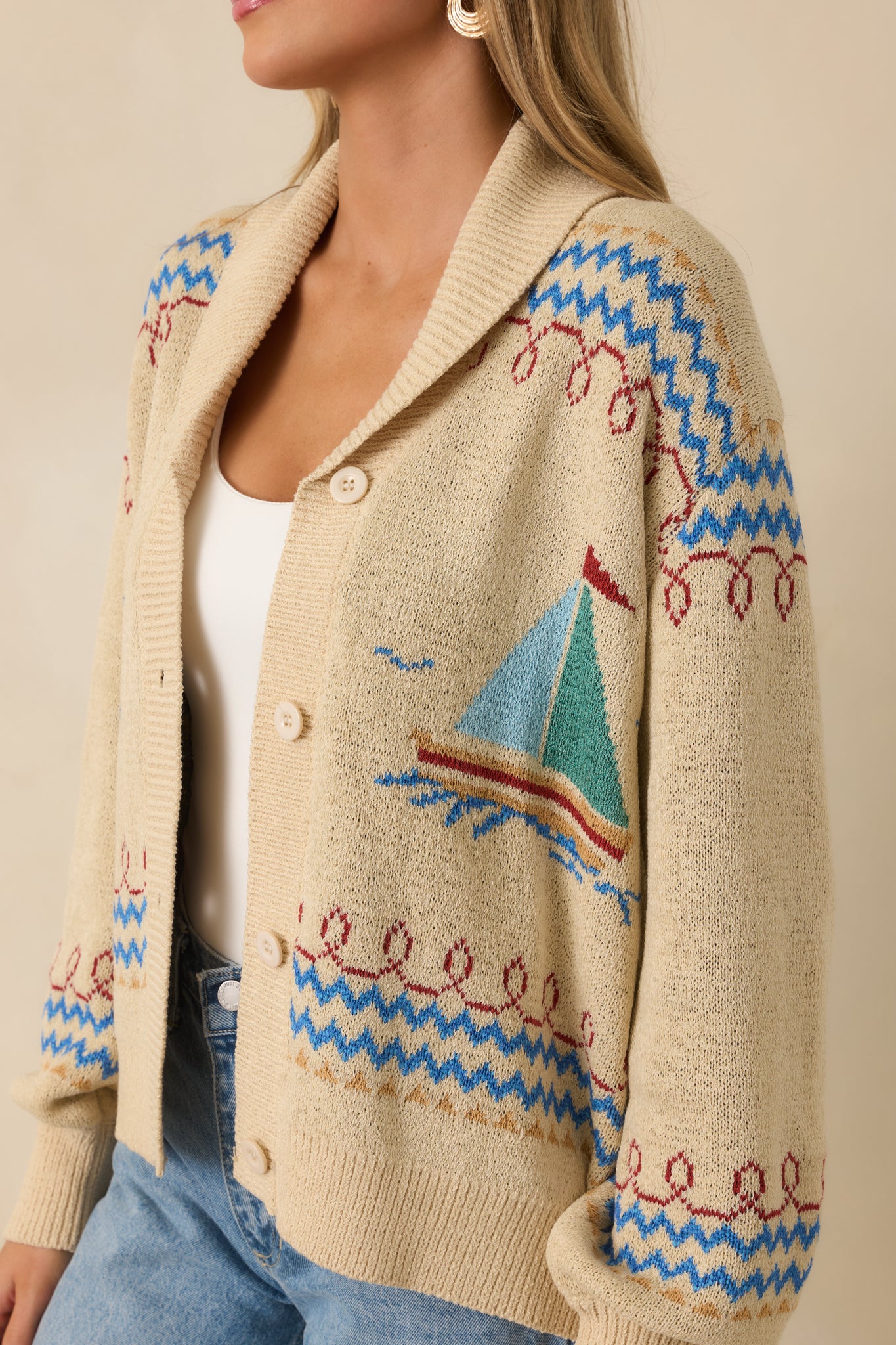 Close-up of the light beige knit fabric showing the sailboat pattern, ribbed trim, and textured stitch detail.