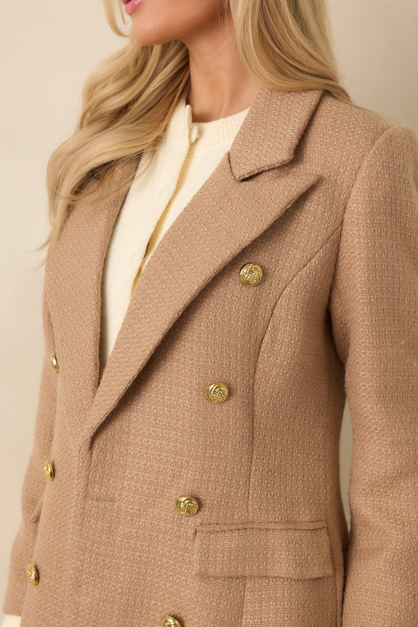 Close-up of the camel coat showing the textured woven fabric, button accents on the cuffs, and flap pocket detailing.