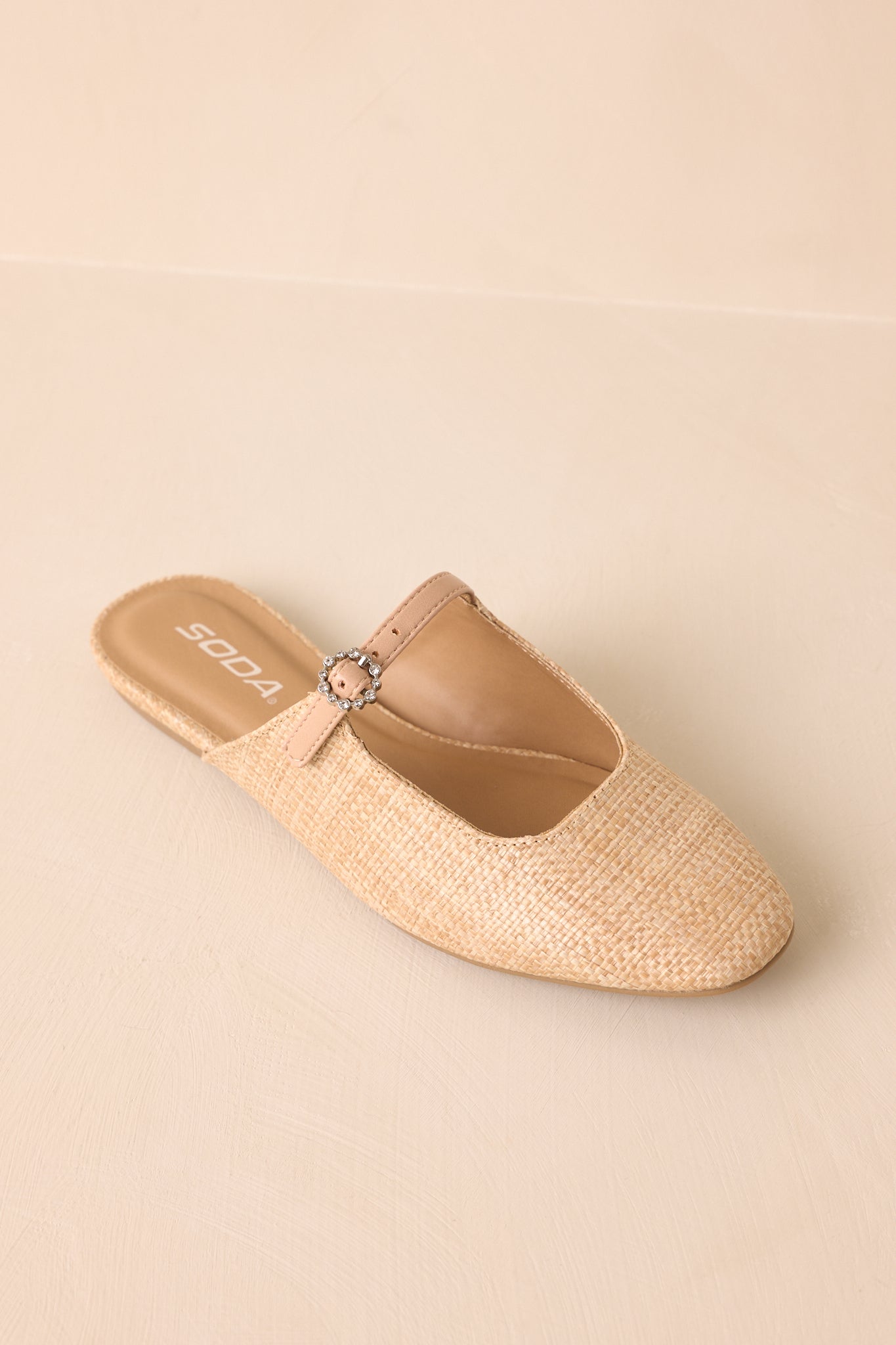Detailed close-up showing the woven raffia upper, strap buckle, and flat sole edge.