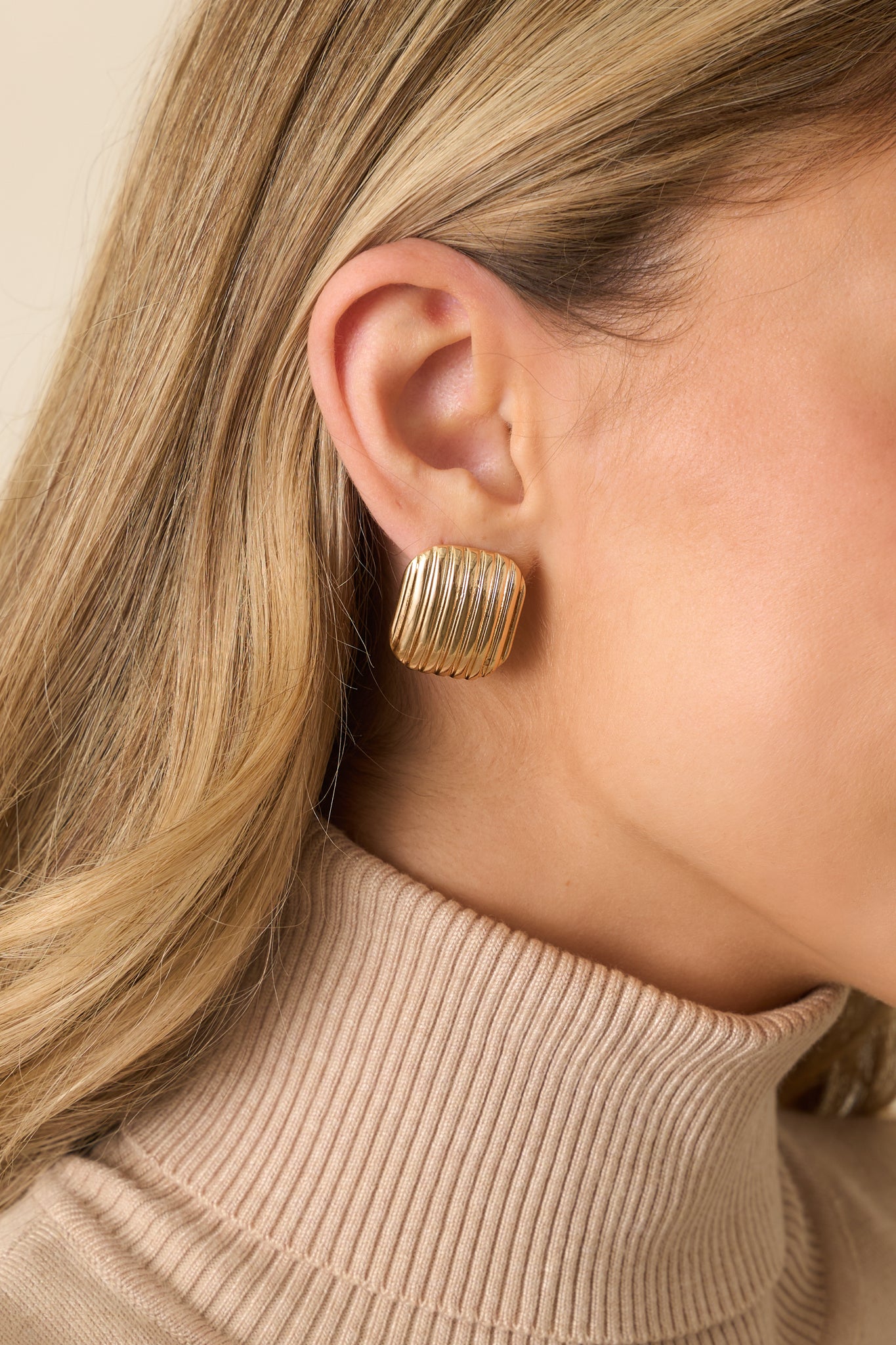 A close-up detail of the square gold earrings showing raised diagonal ridges and secure post back closures.