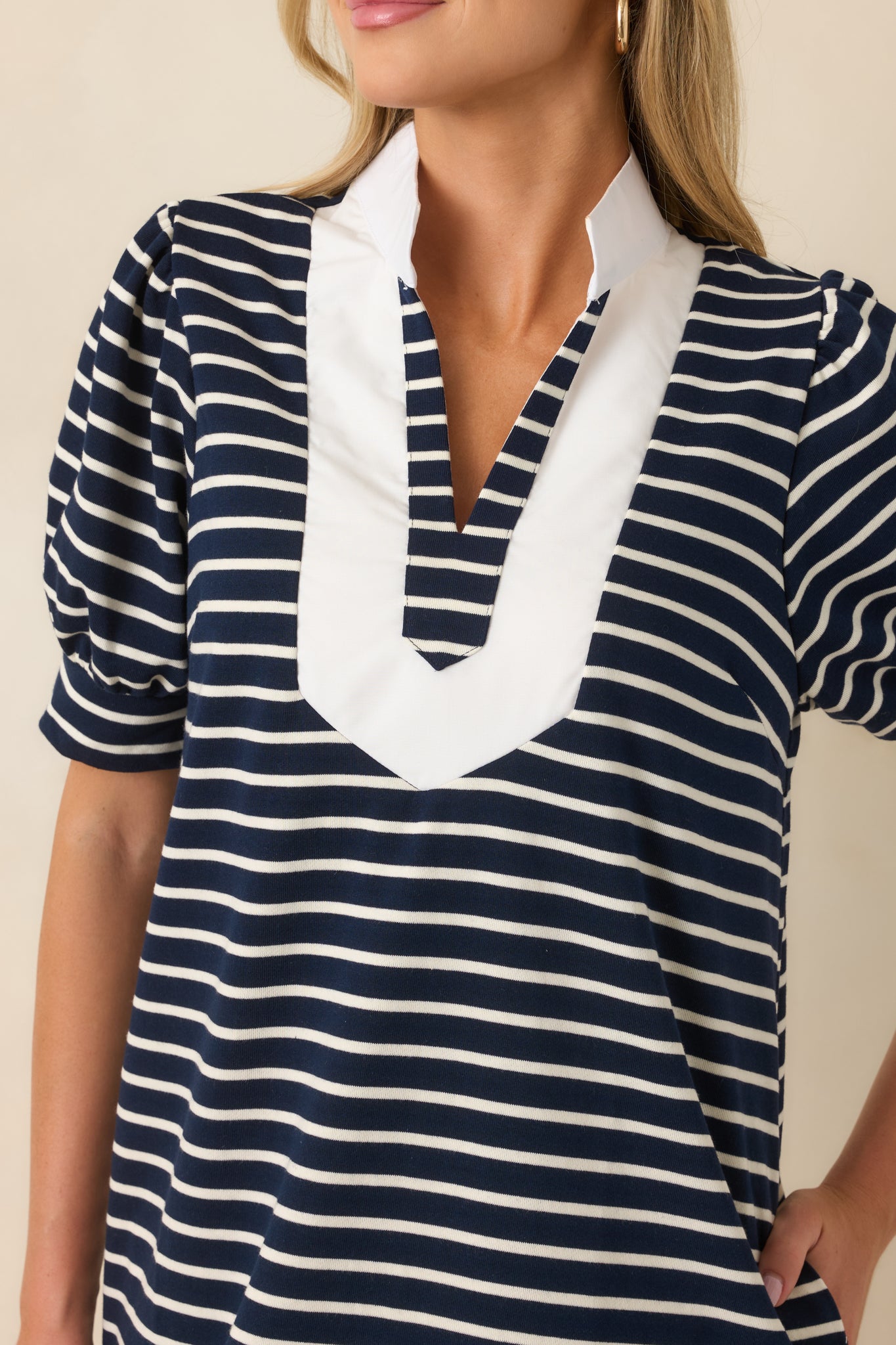 Close-up of the striped mini dress highlighting the split neckline, white contrast trim, soft knit fabric, and puff sleeve detailing.