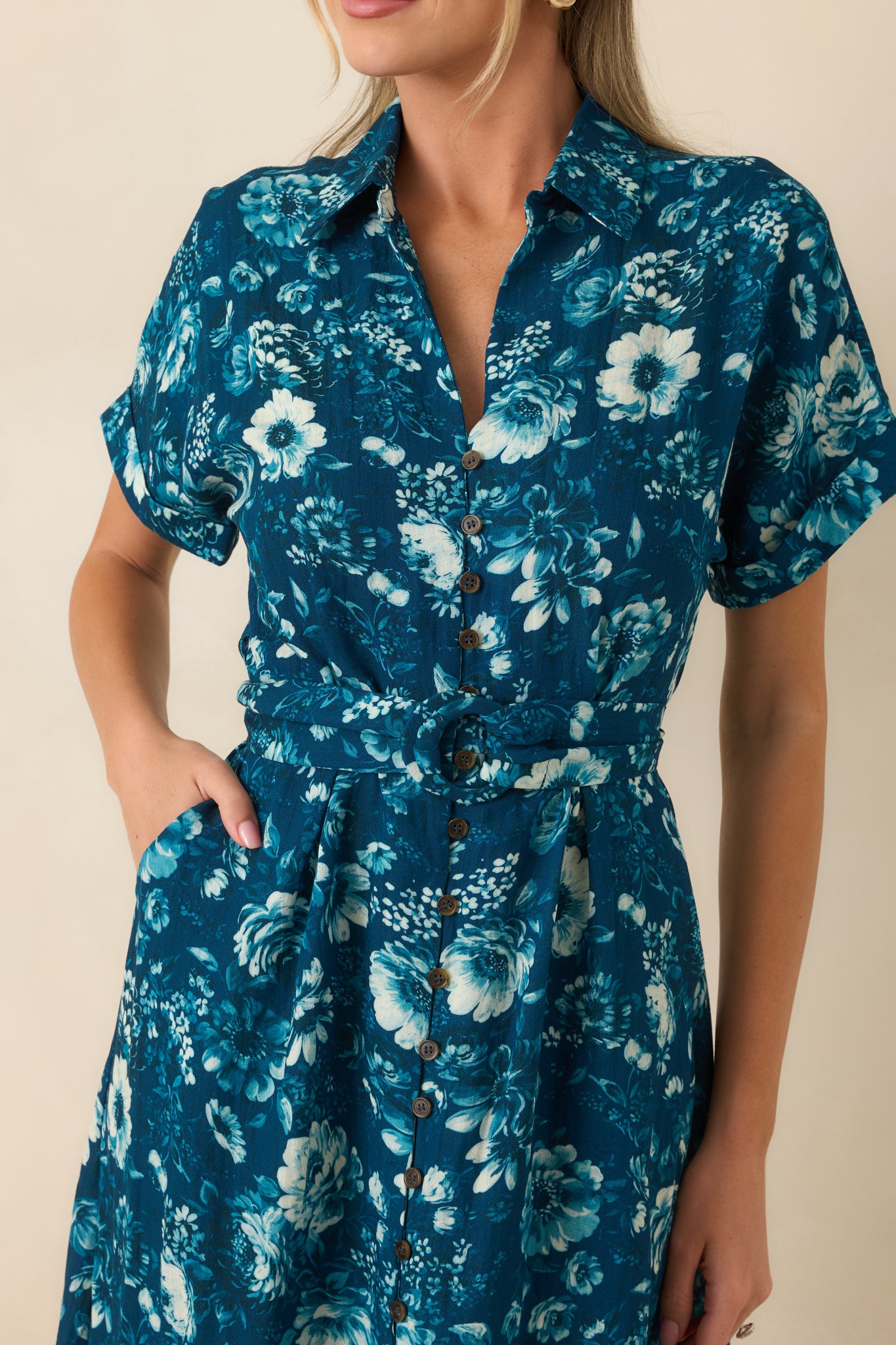 Close-up of the dark teal floral print, collared V-neckline, button front, and belt details.