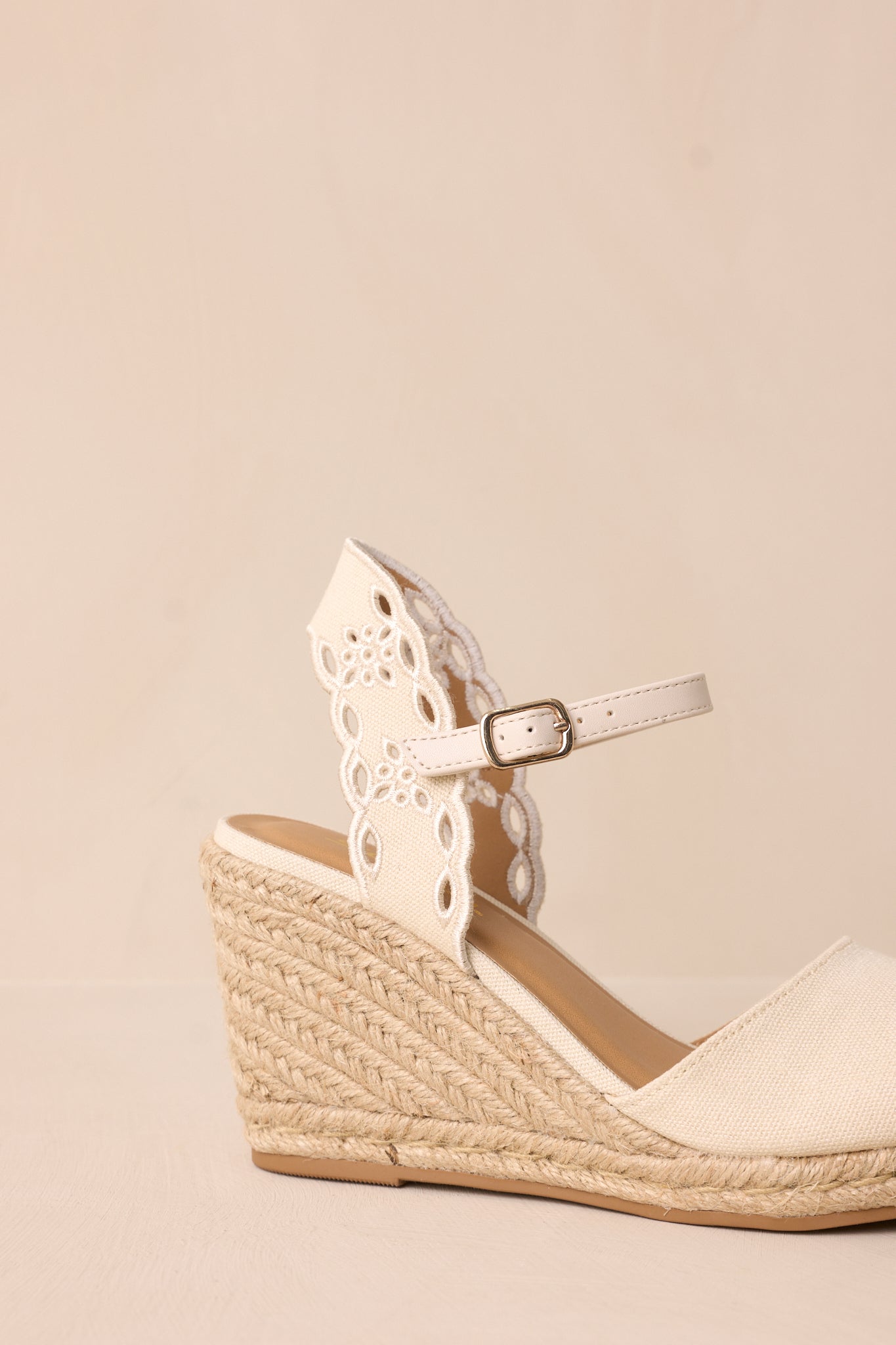 A zoomed-in image focusing on the texture of the woven straw wedge heel, and the intricate floral cutouts on the strap.