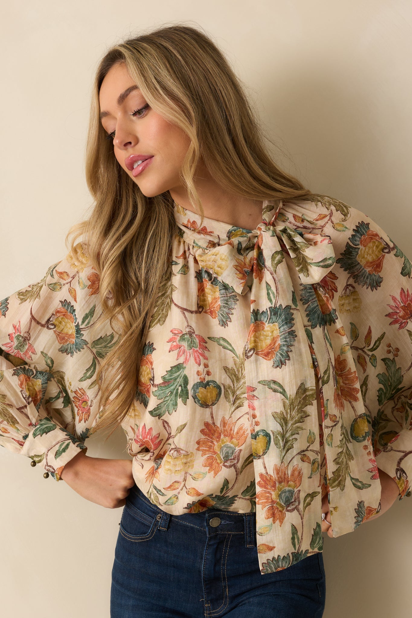 Close view of the bow tie neckline and floral pattern on the beige blouse.