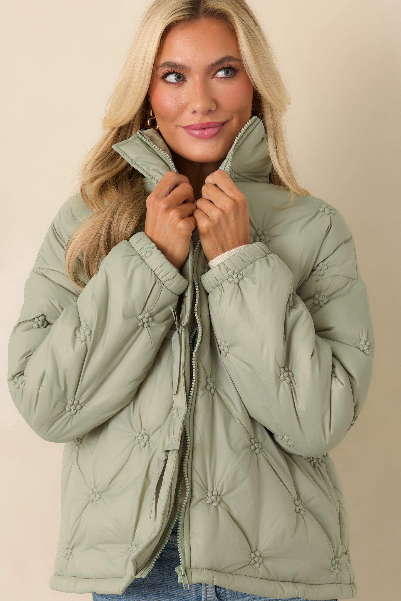 Close view of the sage green jacket front highlighting the zipper closure, floral-inspired quilt pattern, and subtle tie details.