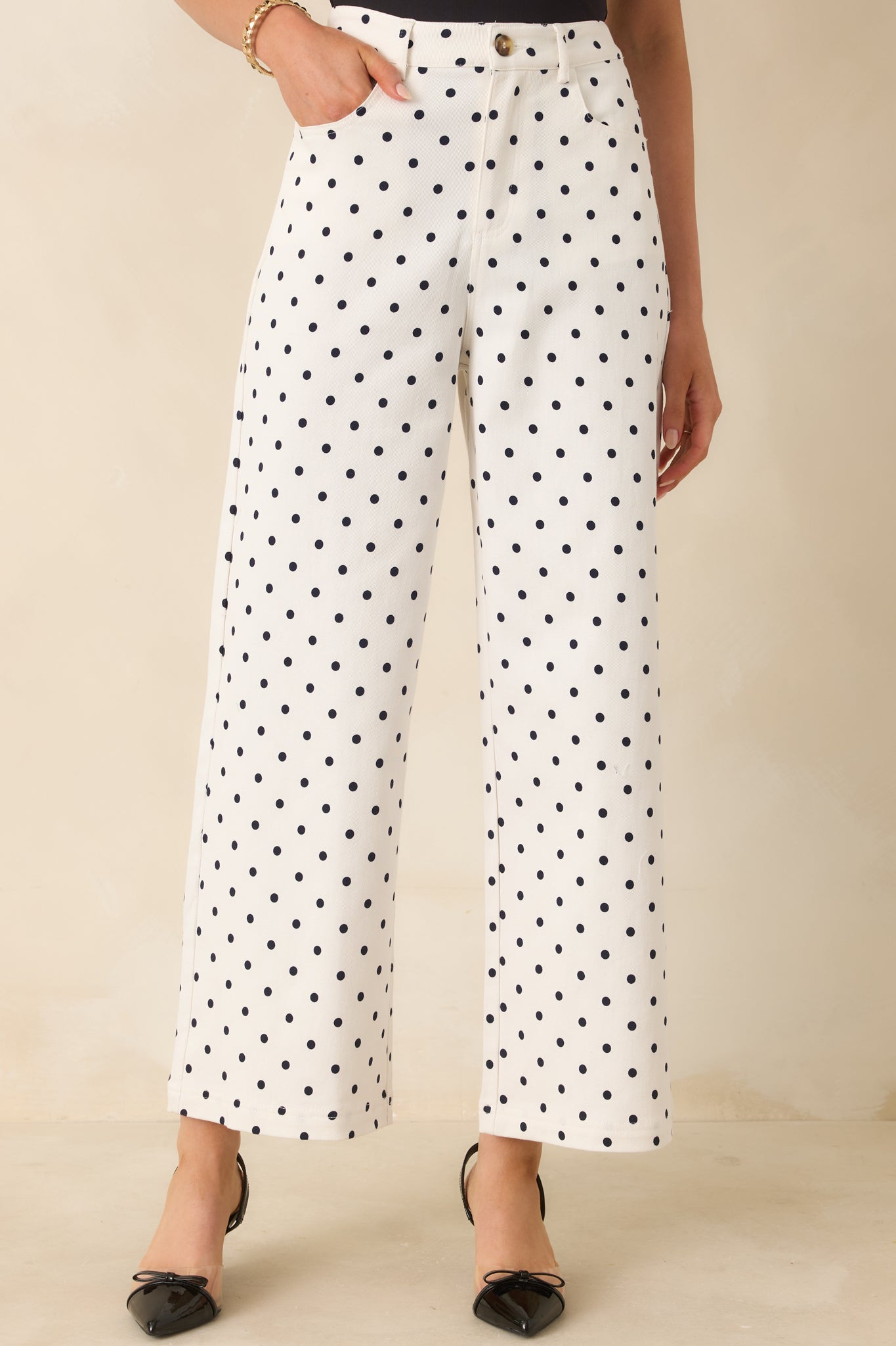 Close view of black polka dot print on soft ivory fabric with smooth straight-leg drape.