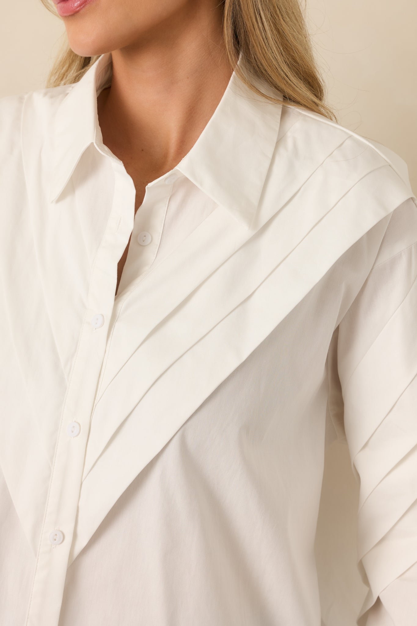 Close view of pleated shoulder stitching and lightweight woven cotton texture on a white blouse.