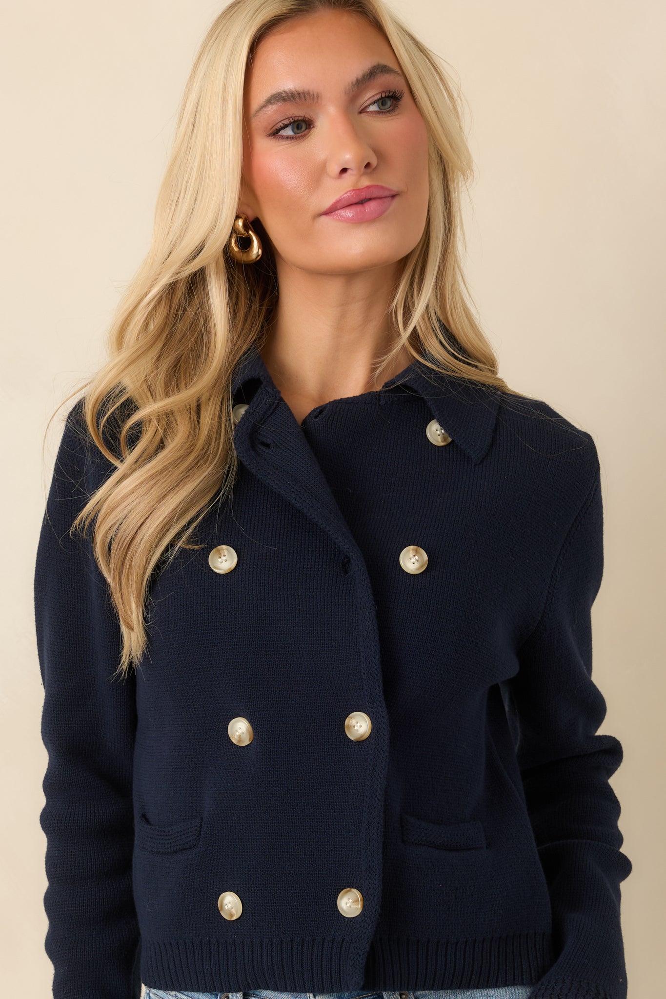 Close view of the double-breasted button front on the navy cardigan with visible stitching and knit texture.