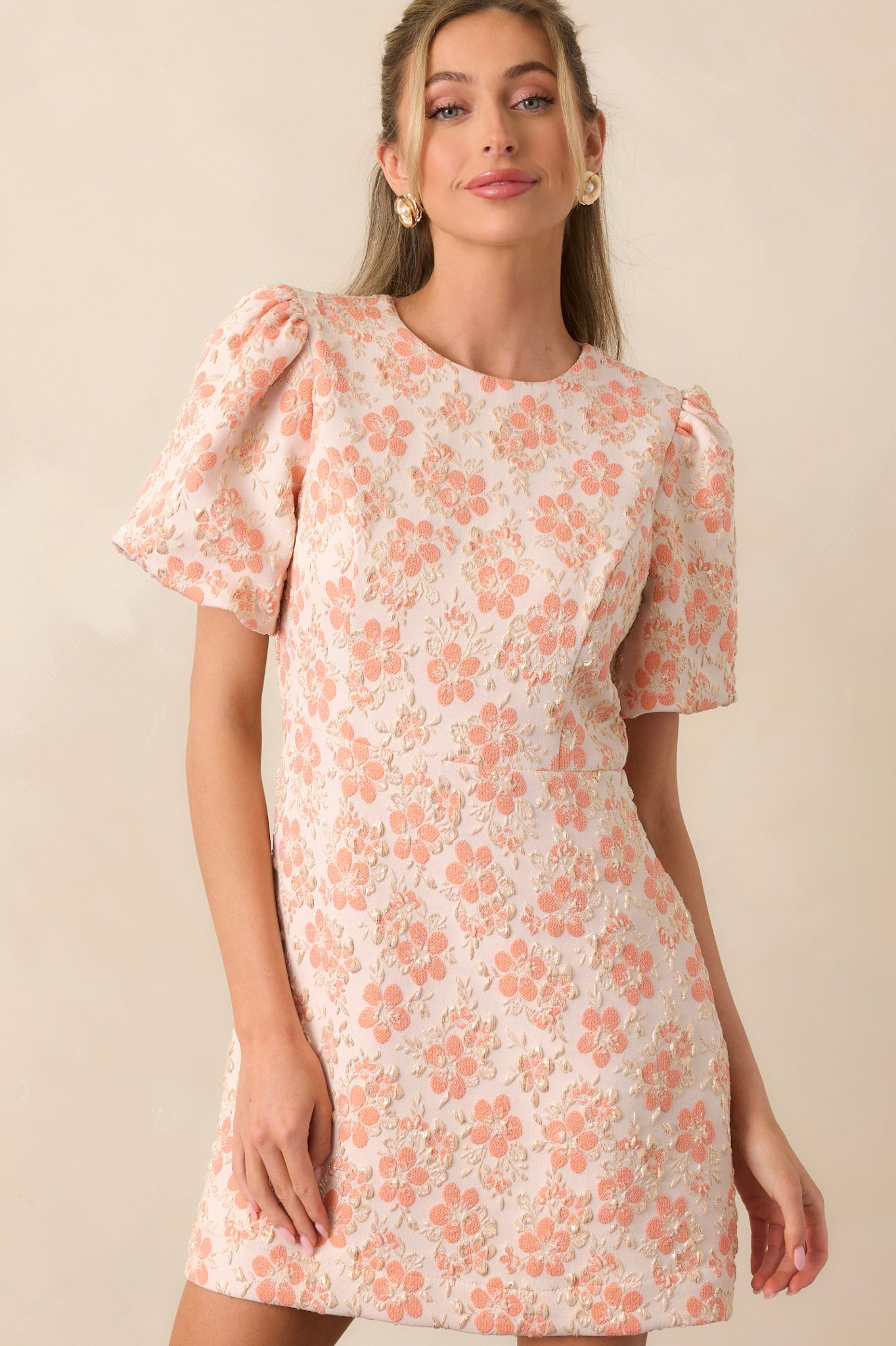 A closer look at the puff sleeves and round neckline of the apricot mini dress, highlighting the gathered fabric and delicate gold embellishments.