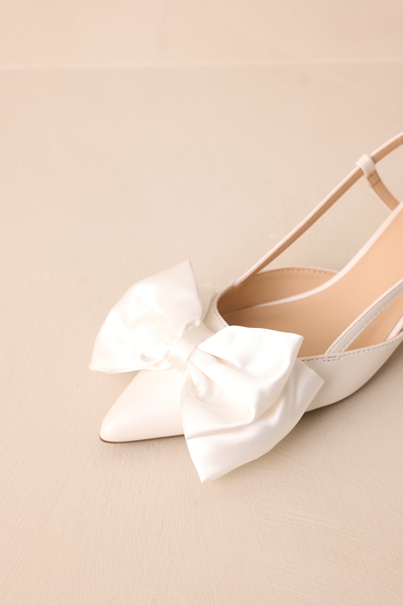 A closer look at the satin bow detail, adding a soft and sophisticated charm to this pointed-toe white heel.