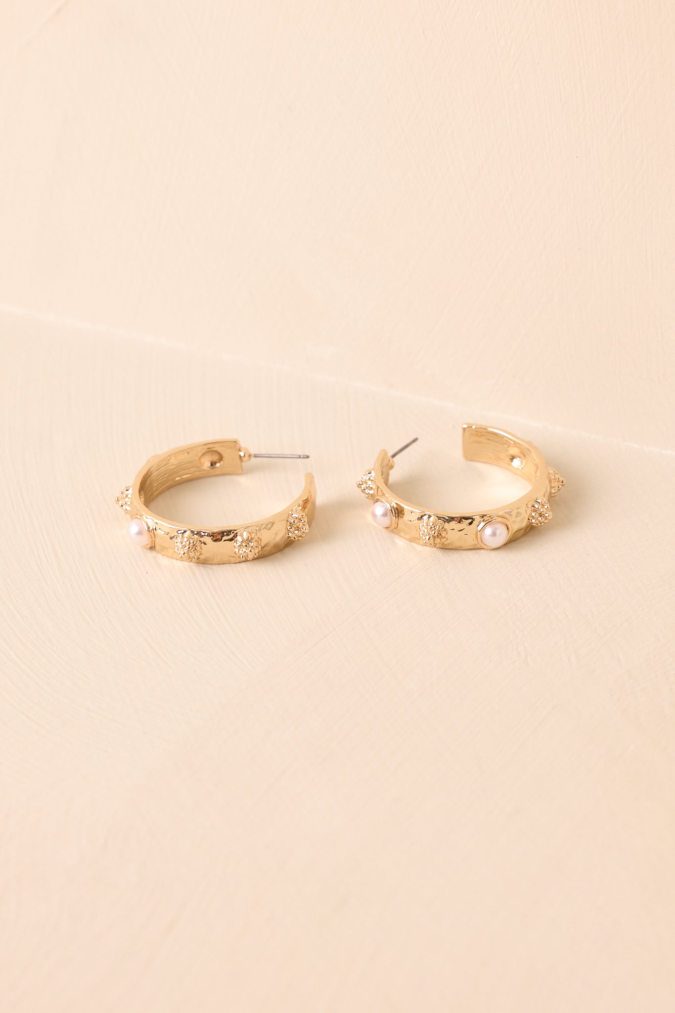 A closer shot of the gold hoop earrings detailing their textured base, bezel-set faux pearls, and half-sphere accents