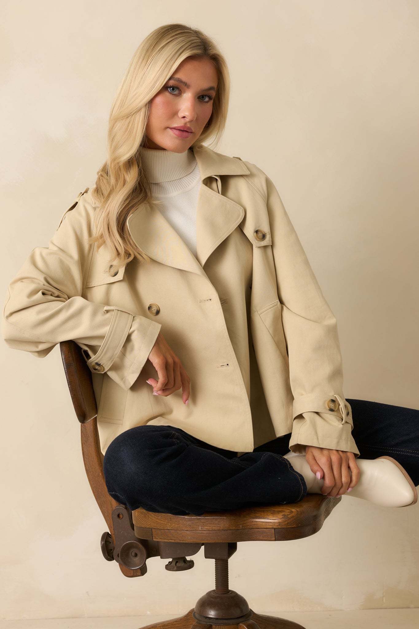 Closer view of the double-breasted buttons and notched collar of the tan trench jacket.