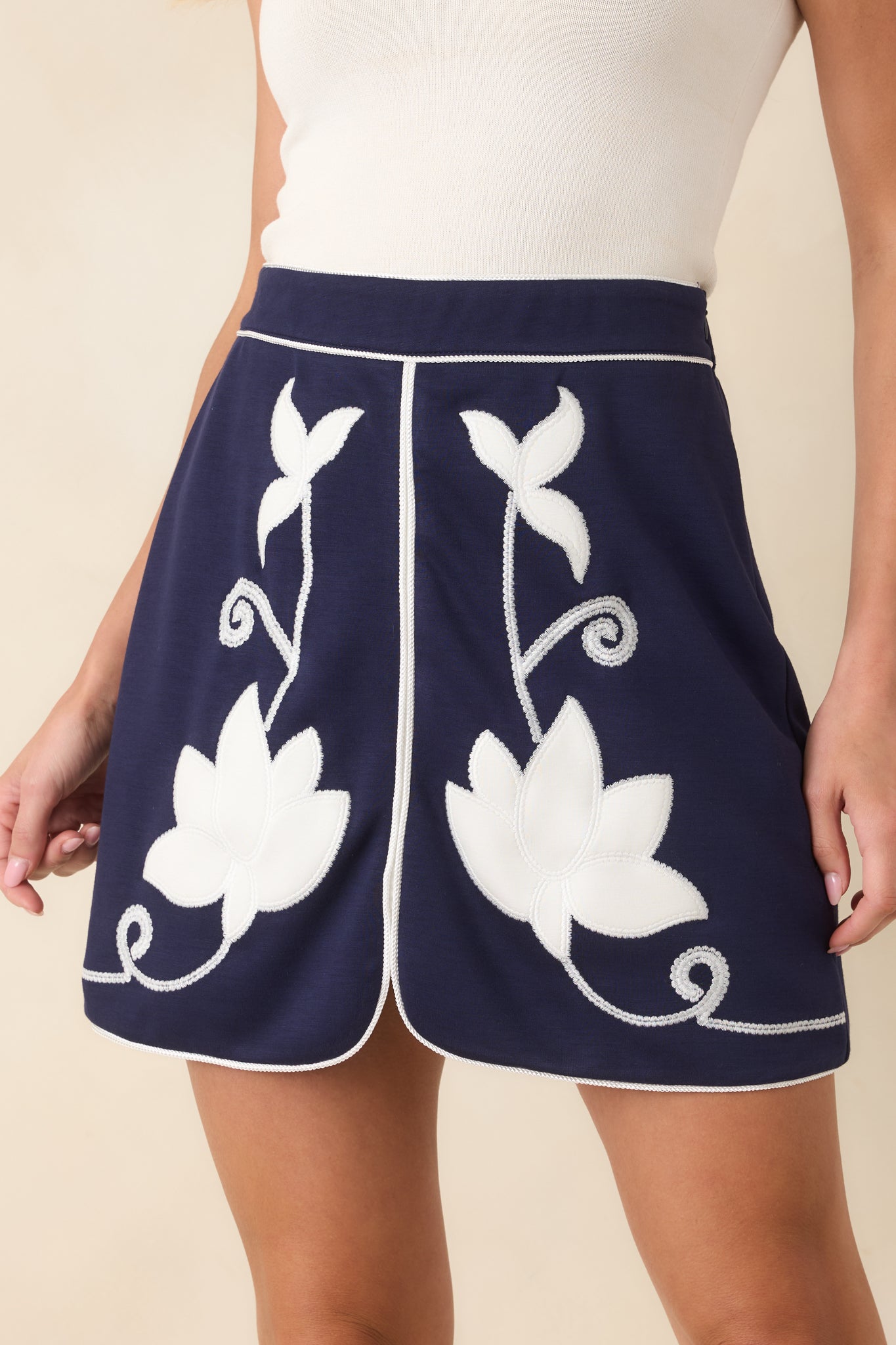 Closer view of the ivory floral appliqué and vine embroidery, highlighting the textured navy fabric and clean piping.