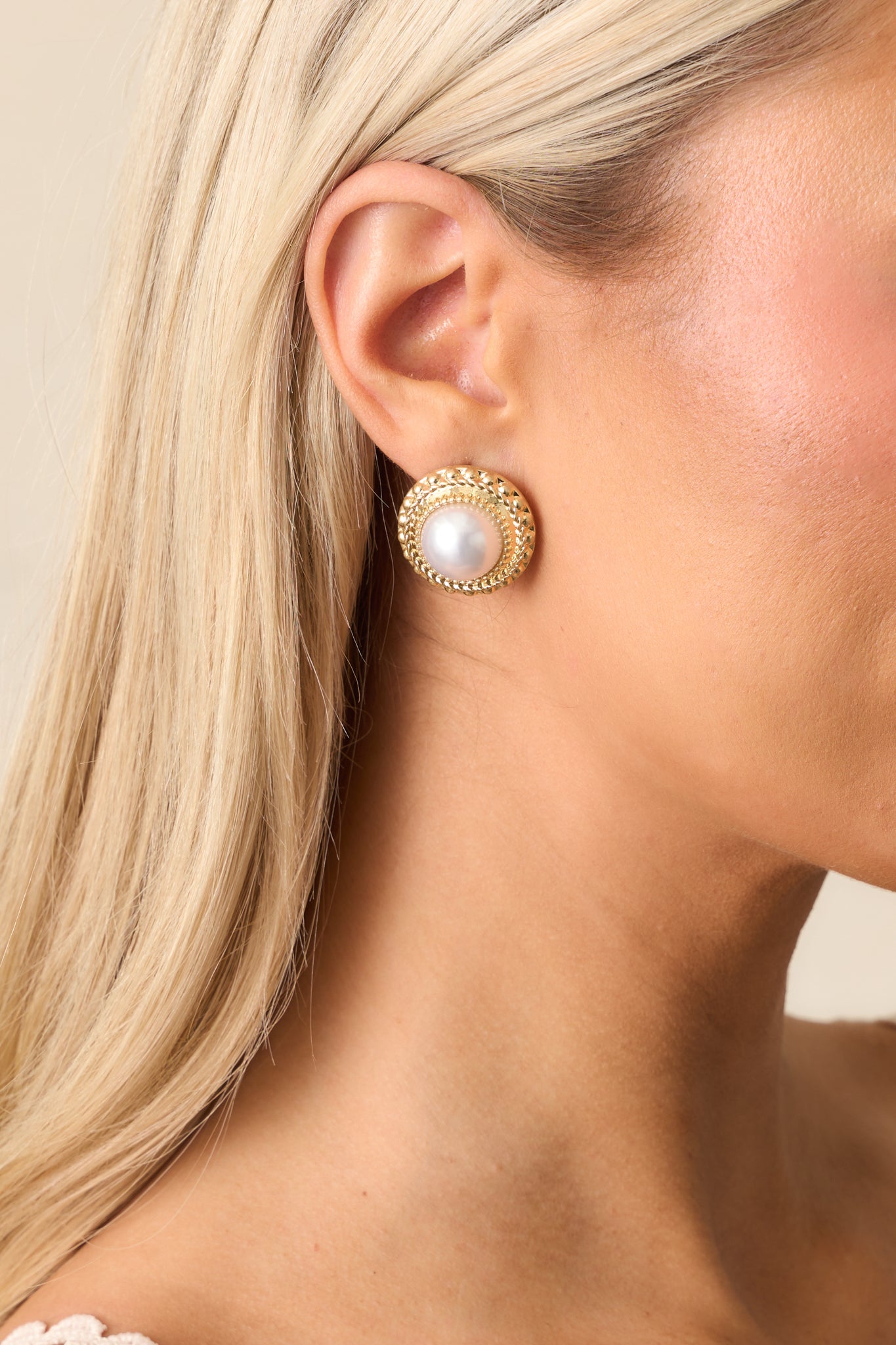 A closer view of the earrings, showcasing the braided gold border on the edge and the elegant ivory pearl centerpiece framed by the textured gold detailing.