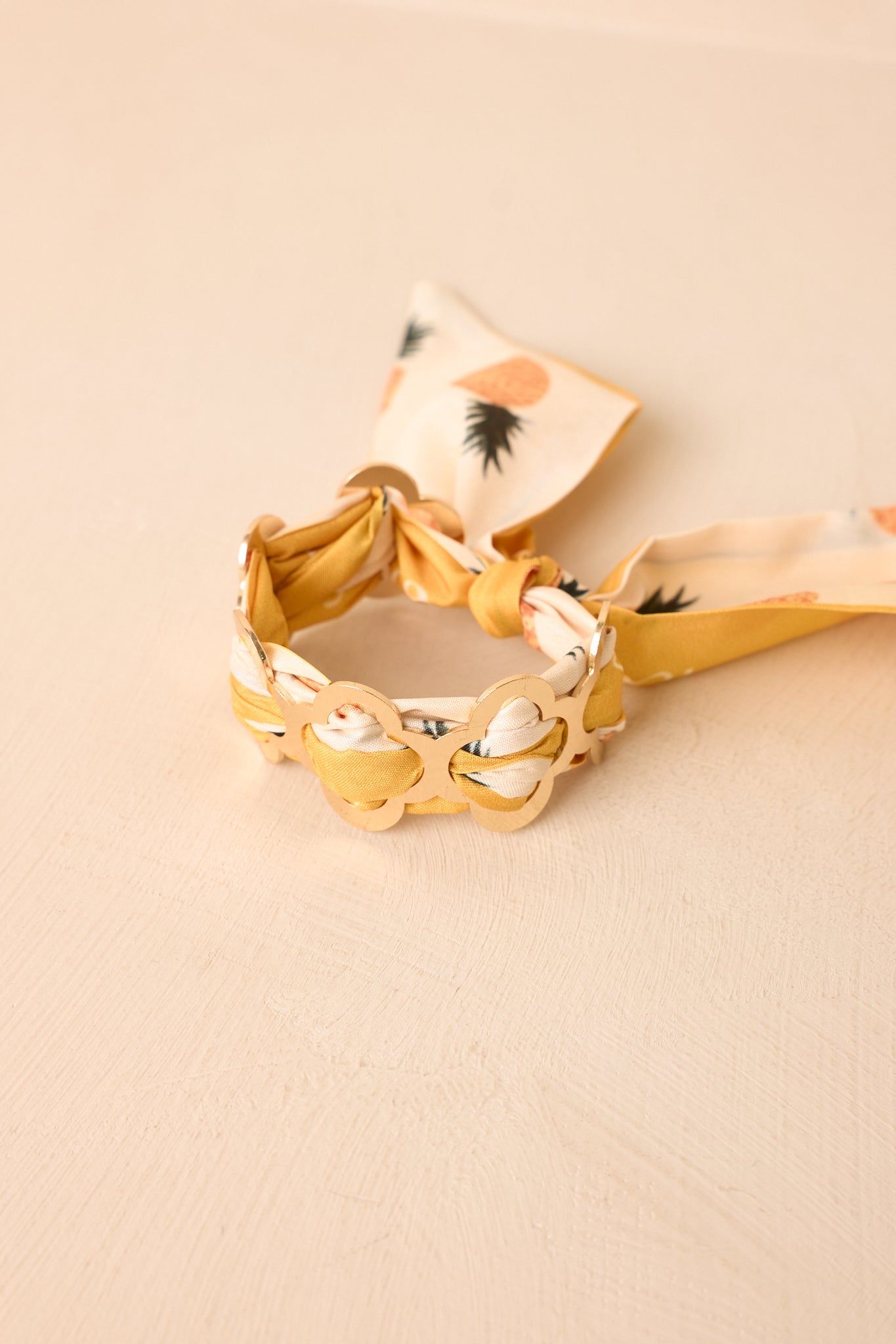 Close-up of the yellow and ivory pineapple-print scarf woven through the geometric gold cuff design.