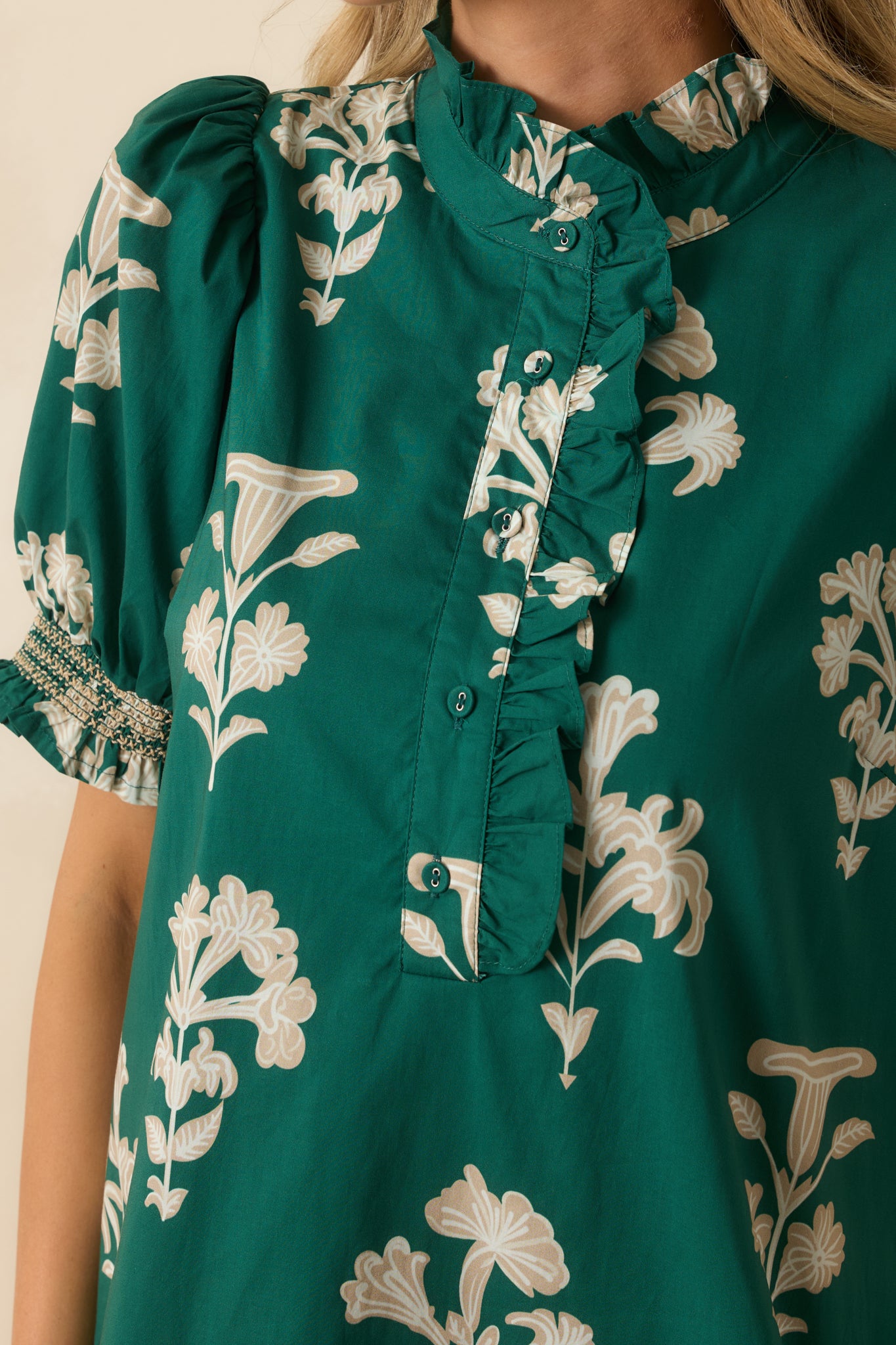 Close-up of the green floral fabric showing the ruffled neckline, gathered detailing, and button placket trim.