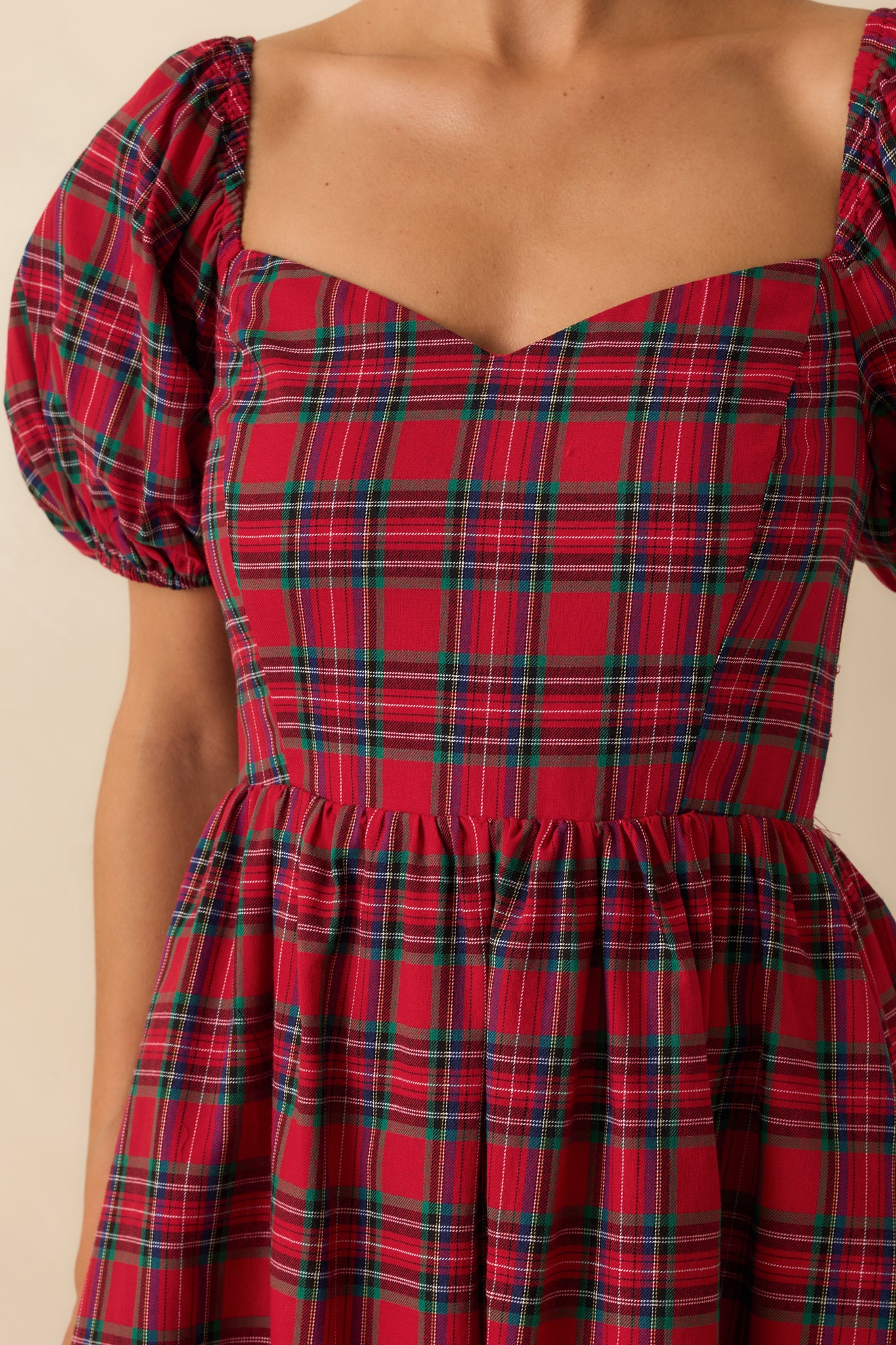 Macro view of the plaid pattern, sweetheart neckline, and puff sleeve detailing on the red dress.