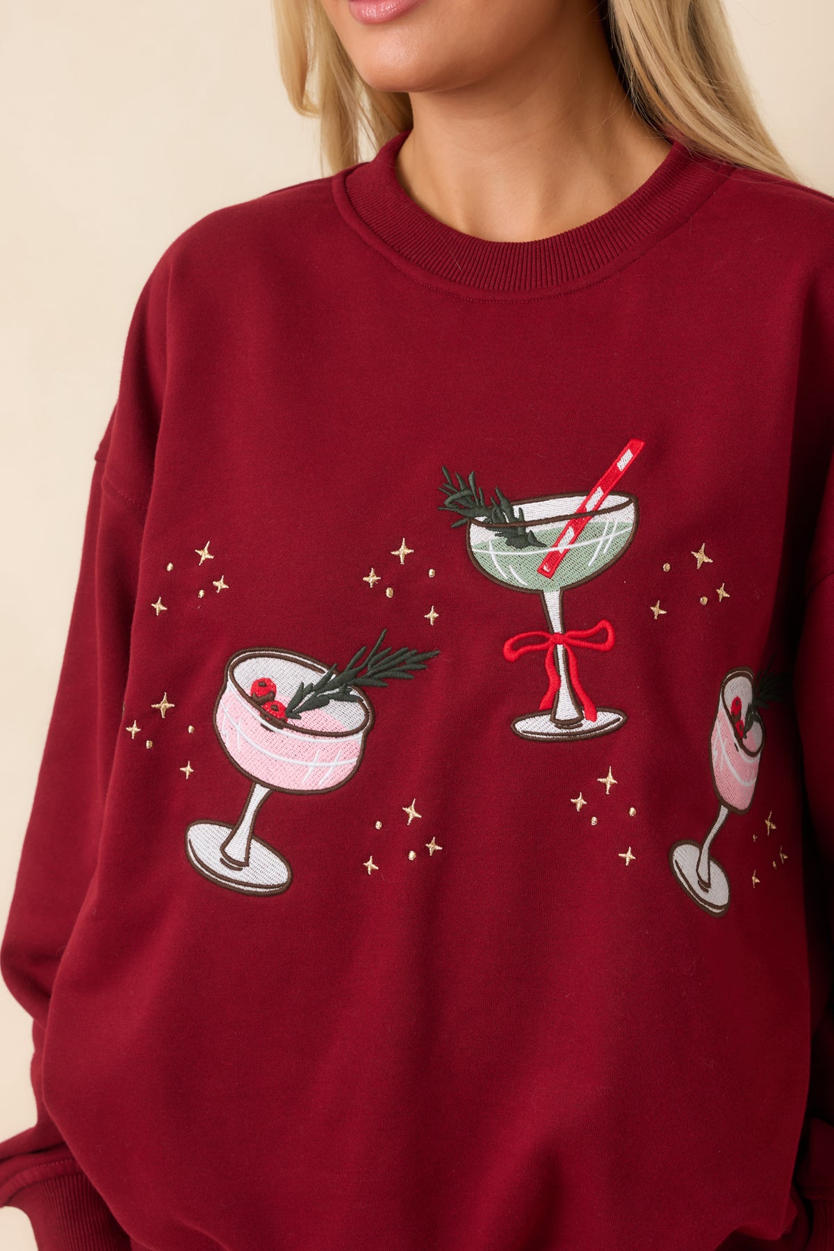 Detailed embroidery of pink and sage cocktail glasses with green foliage, berry accents, a red bow, and gold star embellishments.
