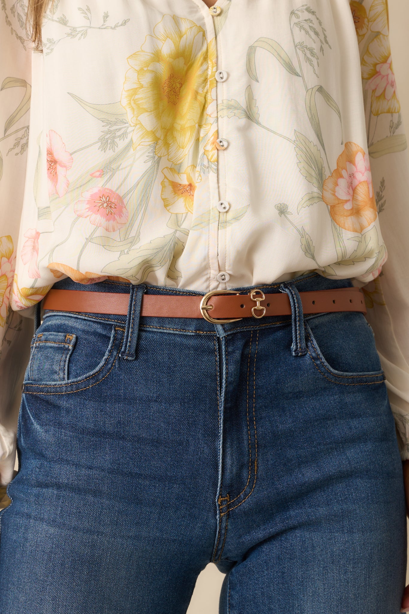 A cropped view of the cognac brown belt showing the polished gold-tone horseshoe buckle and double ring detailing.